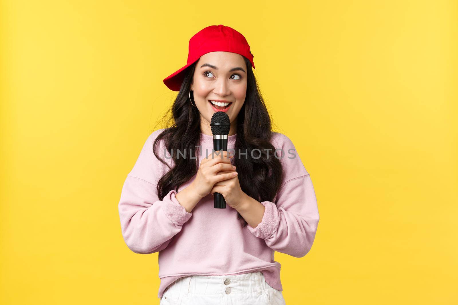People emotions, lifestyle leisure and beauty concept. Dreamy and cute asian girl in red cap, looking upper left corner happy with broad smile, perform stand-up or give speech, singing in microphone by Benzoix
