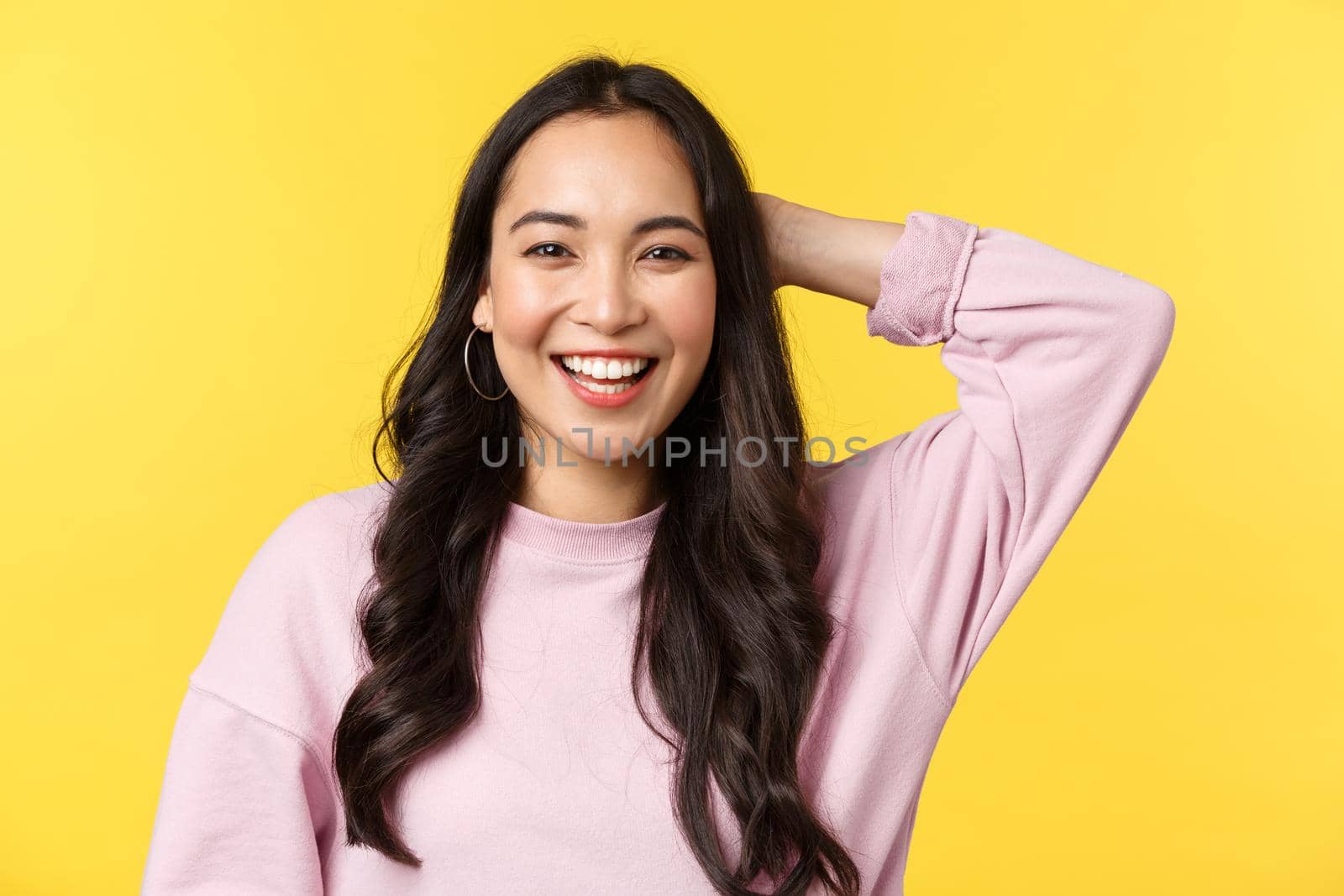 People emotions, lifestyle leisure and beauty concept. Close-up of friendly outgoing cute asian girl laughing and scratch back of head shy, receive praises for good job, stand yellow background.