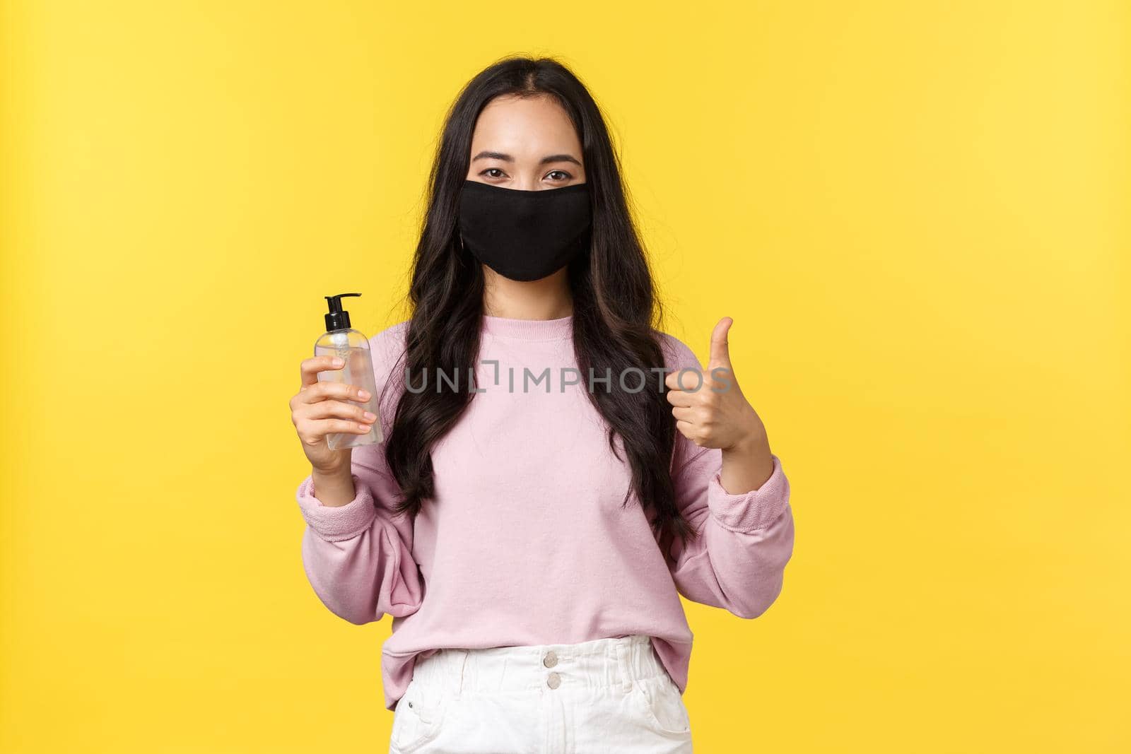 Covid-19, social-distancing lifestyle, prevent virus spread concept. Pretty smiling asian girl in face mask, showing good hand sanitizer and thumbs-up, approve hygiene measures during coronavirus.