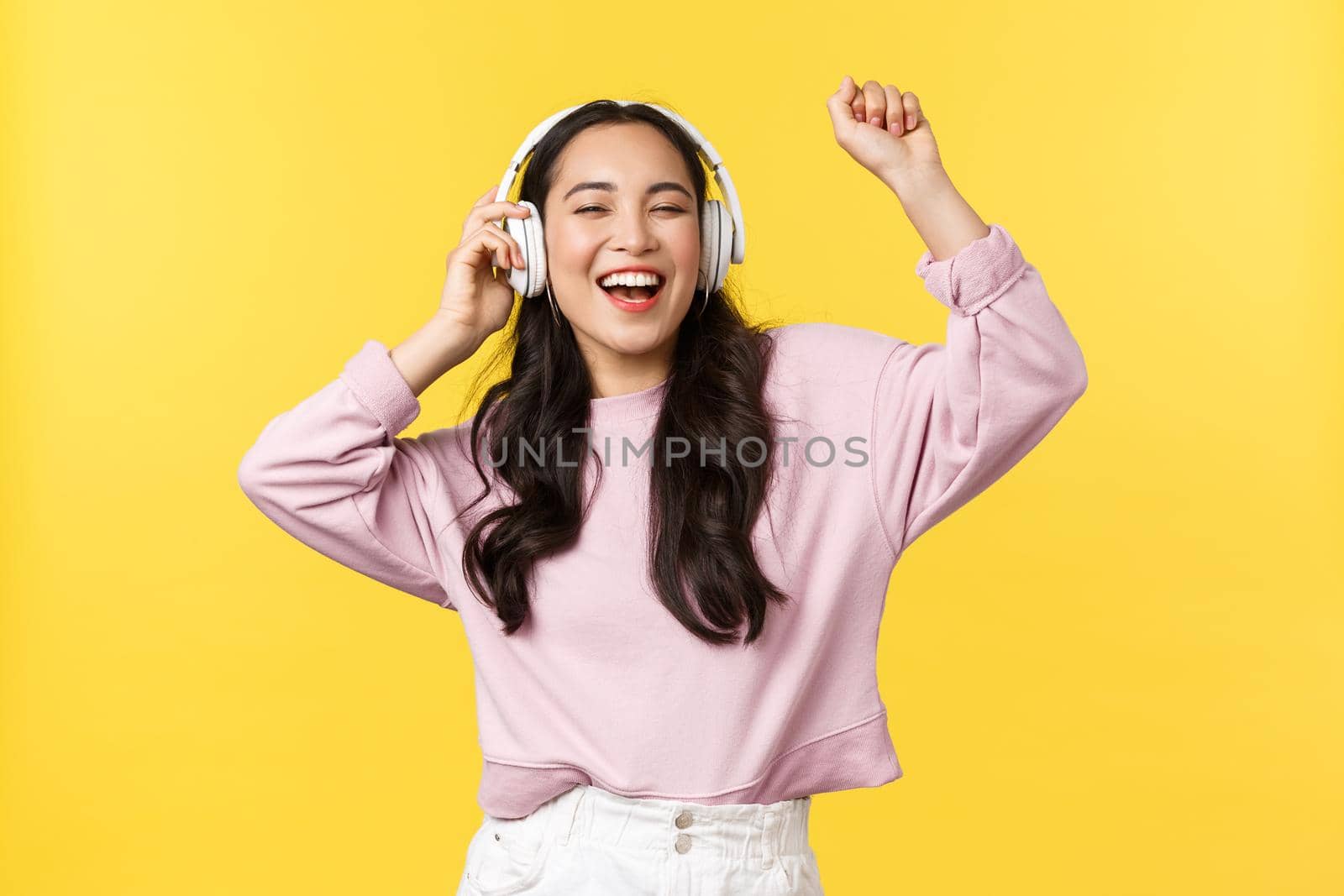 People emotions, lifestyle leisure and beauty concept. Joyful pretty asian woman in wireless headphones listening music, dancing excited with closed eyes and happy smile, listen favorite song by Benzoix