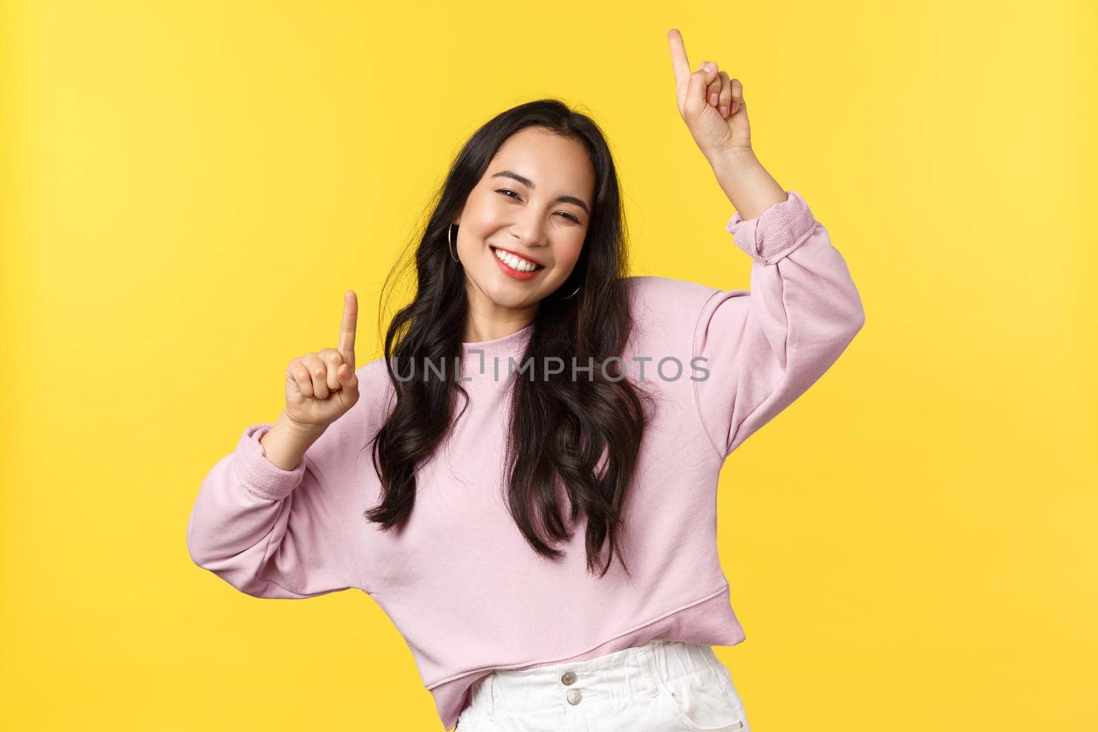 People emotions, lifestyle leisure and beauty concept. Happy carefree attractive korean girl having fun on party, dancing and enjoying summer, raise hands up, smiling broadly, yellow background.