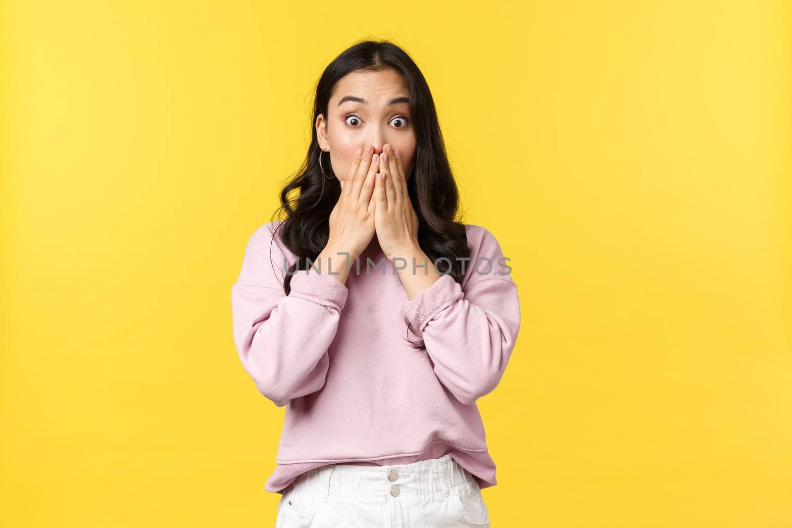 People emotions, lifestyle and fashion concept. Concerned and startled, shocked korean girl in casual outfit, gasping cover mouth hands and look in panic, cant believe own eyes, yellow background.