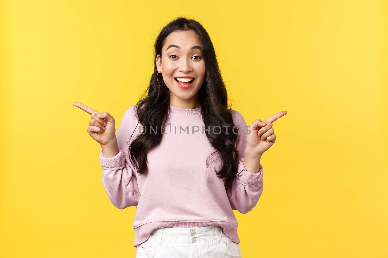 People emotions, lifestyle and fashion concept. Excited young 20s asian woman pointing fingers sideways, showing left and right advertisement, smiling broadly, expressing joy and thrill.