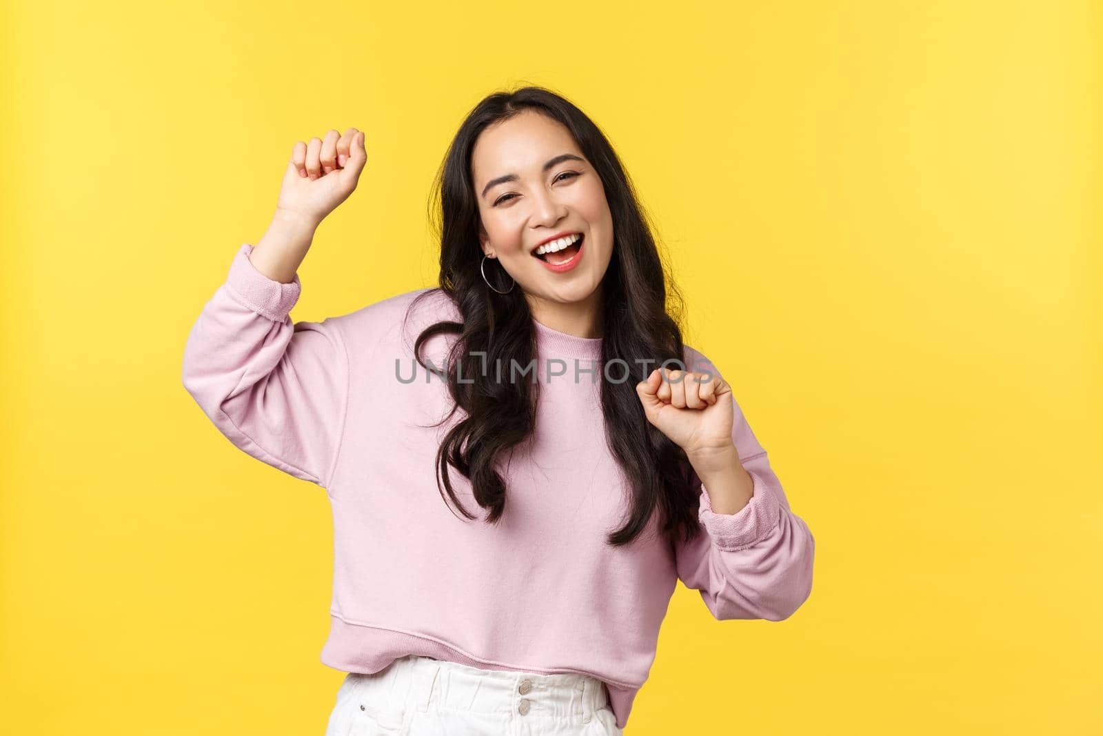 People emotions, lifestyle leisure and beauty concept. Upbeat happy and cheerful asian girl dancing and having fun, partying, moving rhythm music and smiling over yellow background by Benzoix