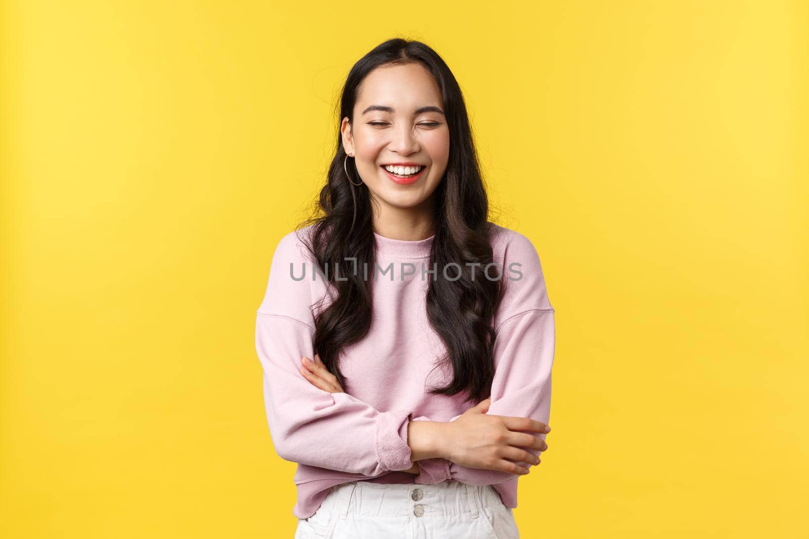 People emotions, lifestyle and fashion concept. Cheerful good-looking korean girl having fun, laughing out loud and feeling happy, standing joyful over yellow background.