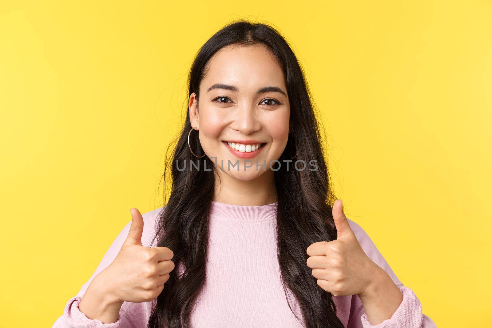 People emotions, lifestyle leisure and beauty concept. Upbeat smiling asian girl showing thumbs-up in approval, standing yellow background, agree and support idea, yellow background.