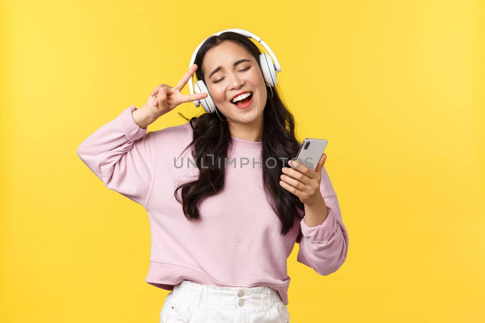 People emotions, lifestyle leisure and beauty concept. Carefree good-looking asian woman close eyes and dancing relaxed with smartphone, listening music in headphones, singing karaoke.