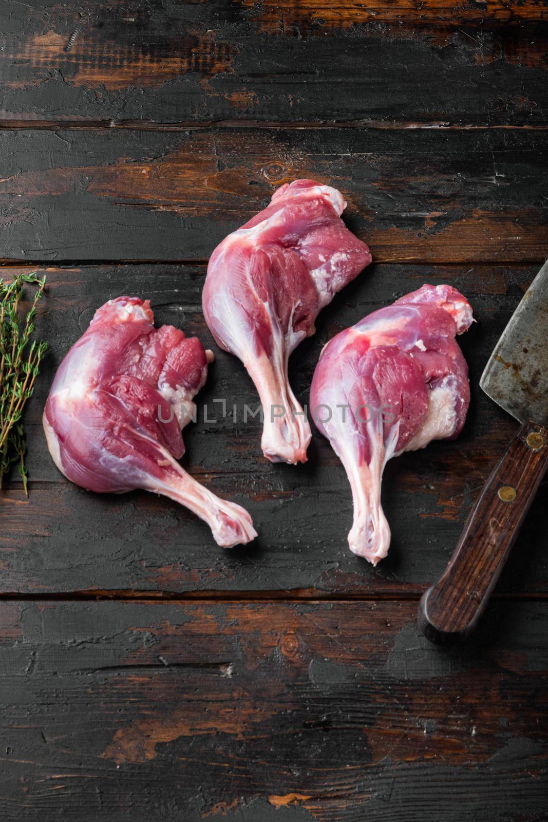 Raw meat, duck legs set with old butcher cleaver knife, on old dark wooden table background, top view flat lay, with copyspace and space for text