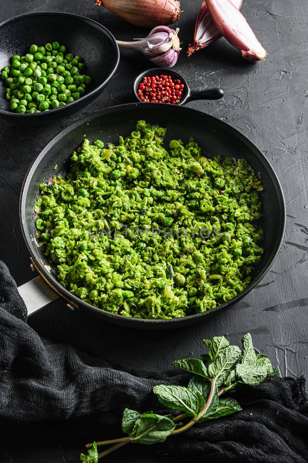 english mushy peas recipe cooked frying pan and peas in bowl with mint shallot pepper and salt over black stone surface organic keto food side view.