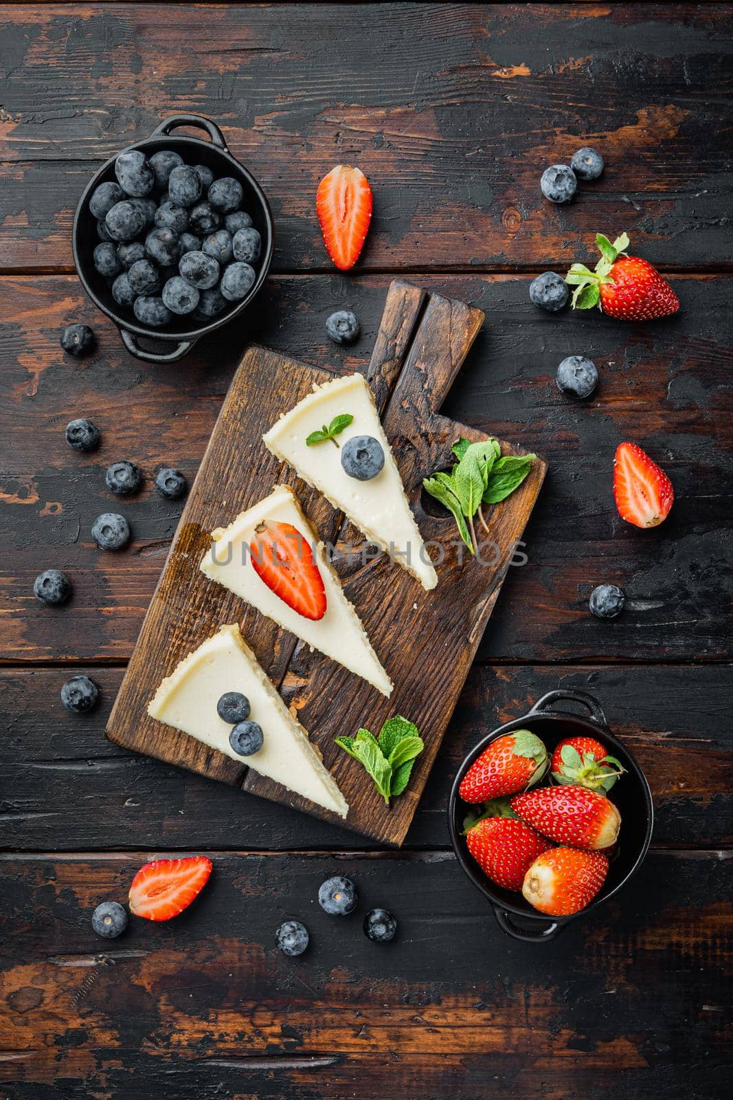 Slice of cheesecake with strawberries, blueberry and mint, on old dark wooden table background, top view flat lay