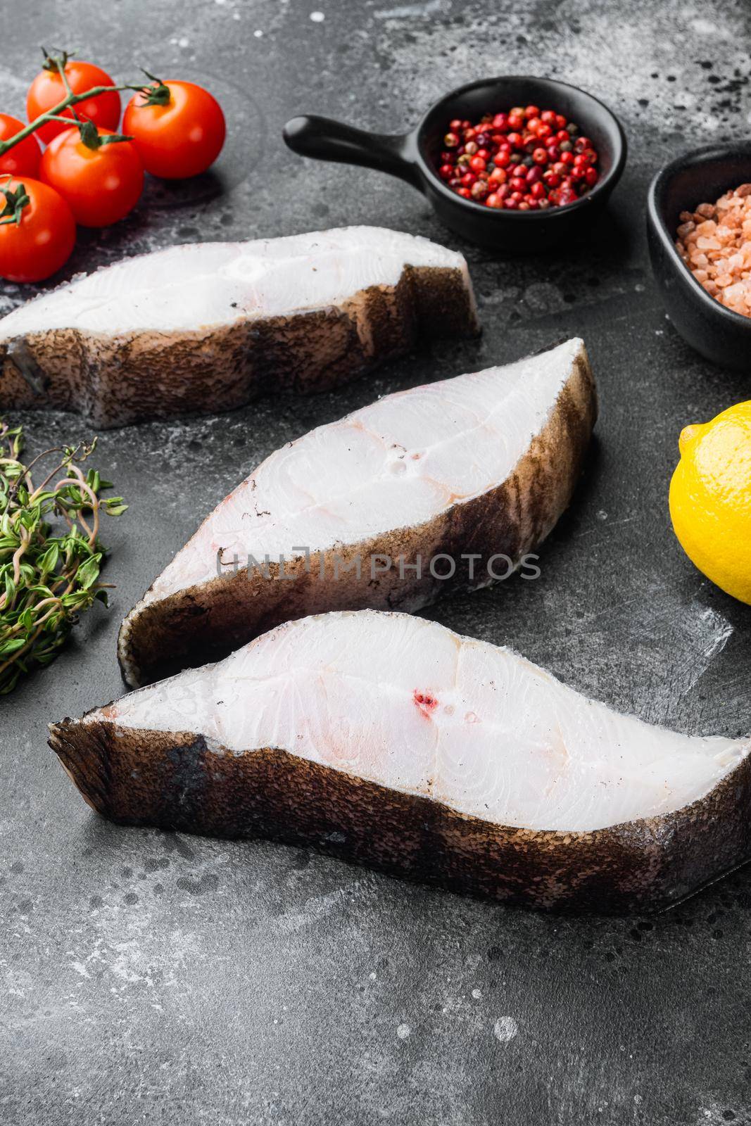 Raw halibut saltwater fish steak, with ingredients and rosemary herbs, on black dark stone table background by Ilianesolenyi