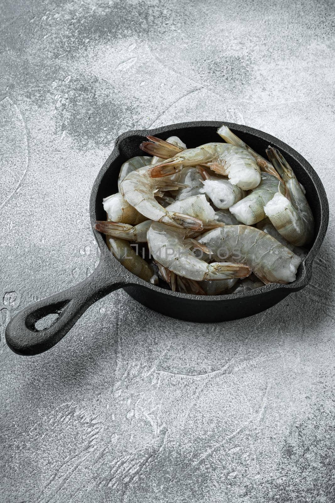 Raw fresh uncooked prawns shrimps set, in cast iron frying pan, on gray stone background, with copy space for text