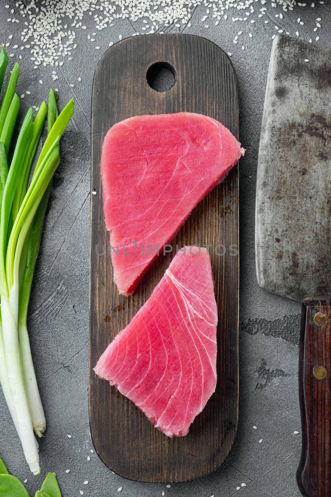 Fresh raw tuna fish steak with green pea, sesame and spring onions, on wooden cutting board, and old butcher cleaver knife, on gray stone background, top view flat lay by Ilianesolenyi