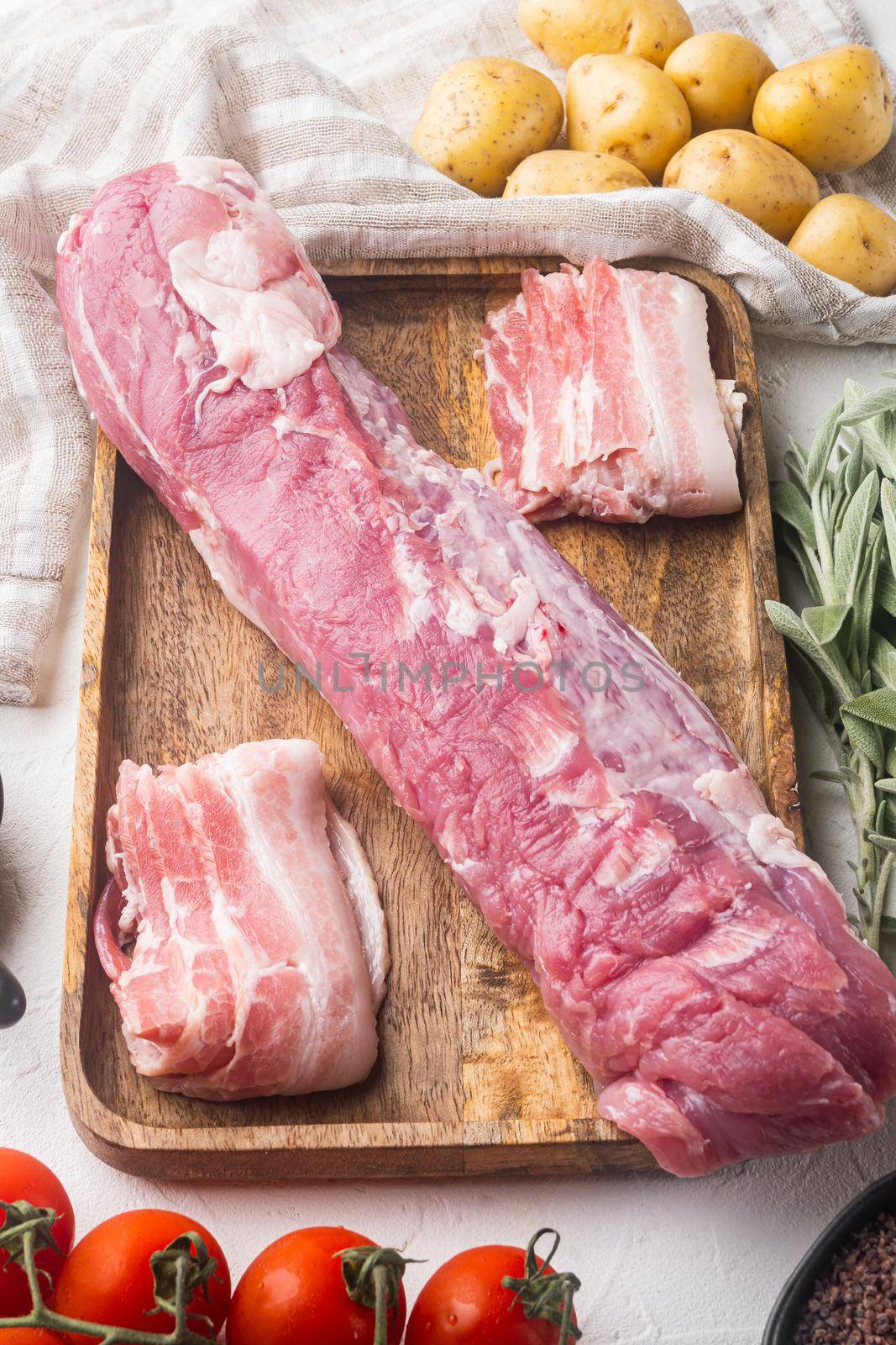 Raw pork loin with ingredients and herbs for baking, sage, potatoe set, on wooden tray, on white stone background