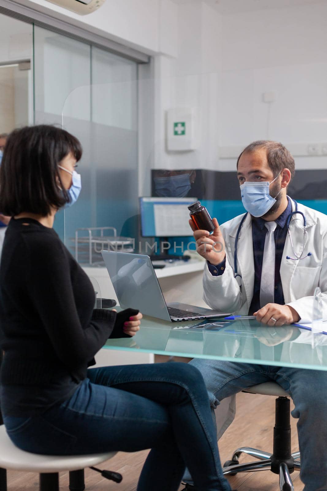 Specialist giving bottle of prescription pills to patient for treatment, doing checkup consultation in cabinet. Woman receiving flask of medicaments from medic during covid 19 pandemic.