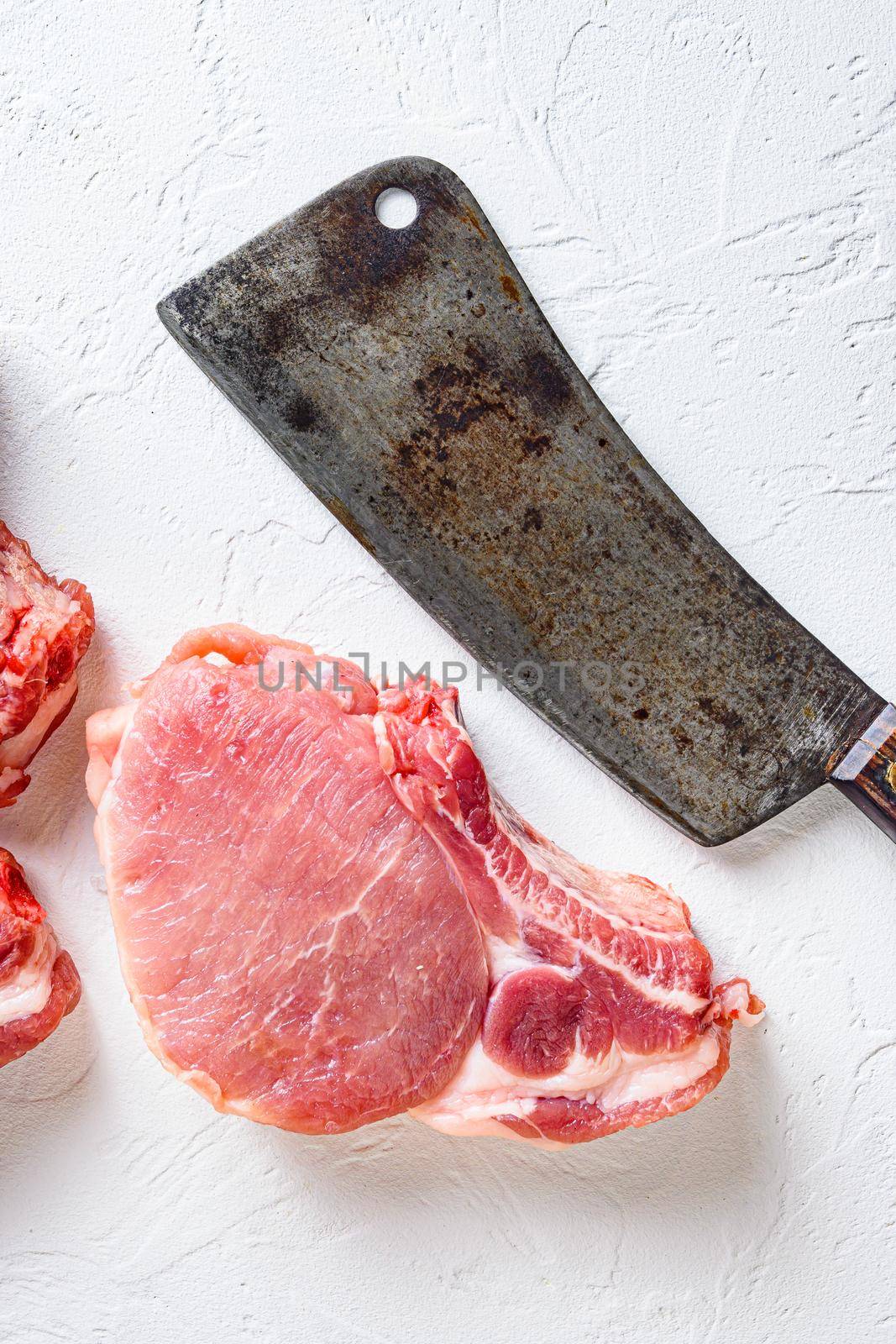 Organic bio Raw pork chops set for grilling, baking or frying, Fith butcher cleaver ower textured white background. top view.
