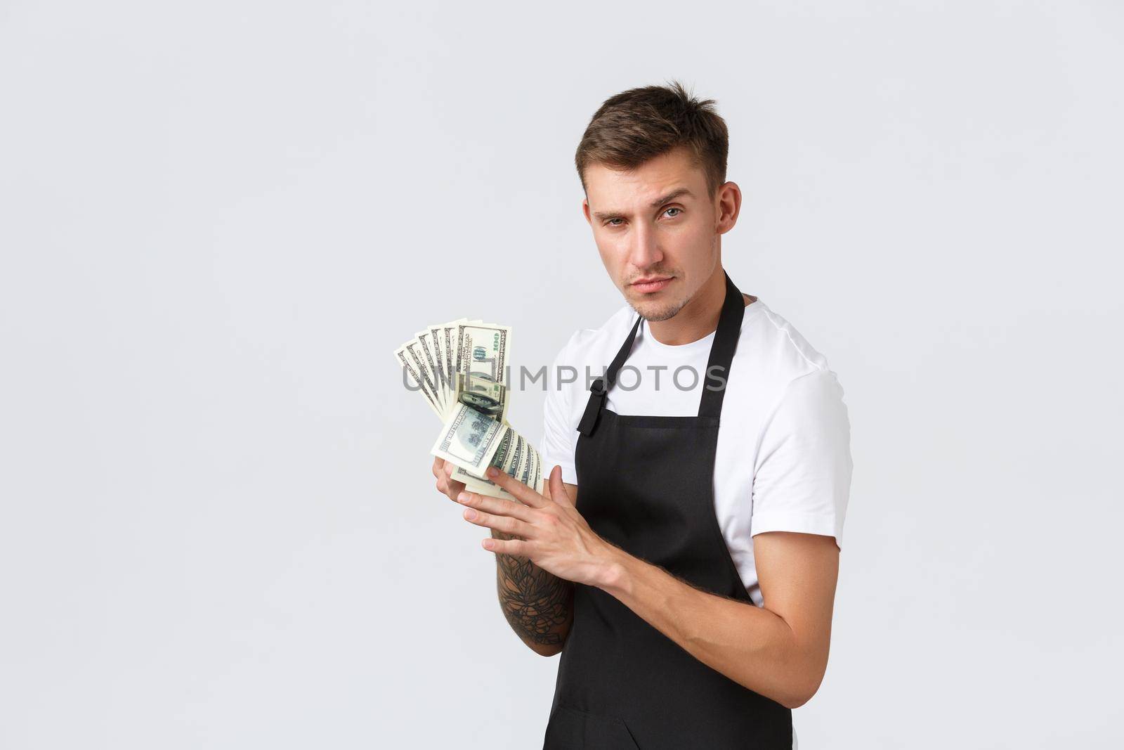 Small retail business, payments and employees concept. Cheeky handsome salesman, cafe owner counting income, showing money and smiling satisfied, standing white background.