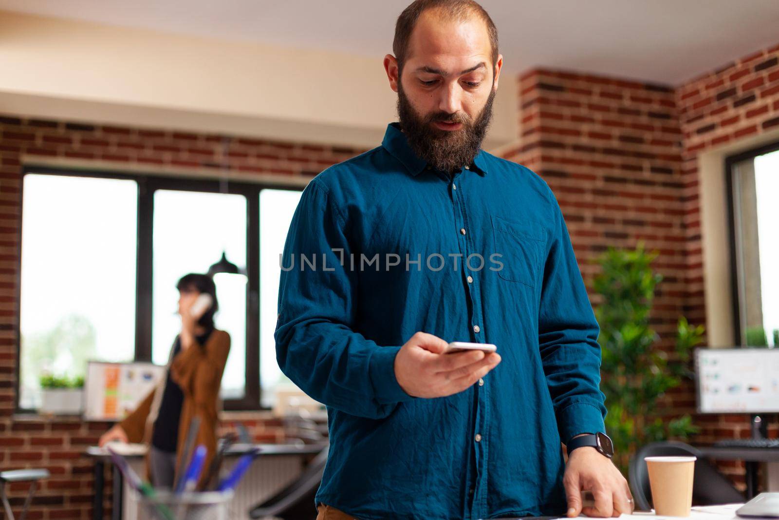 Businessman holding modern smartphone waiting for imporant call looking at watch time while working at business presentation in startuo office. Executive manager analyzing marketing strategy papers