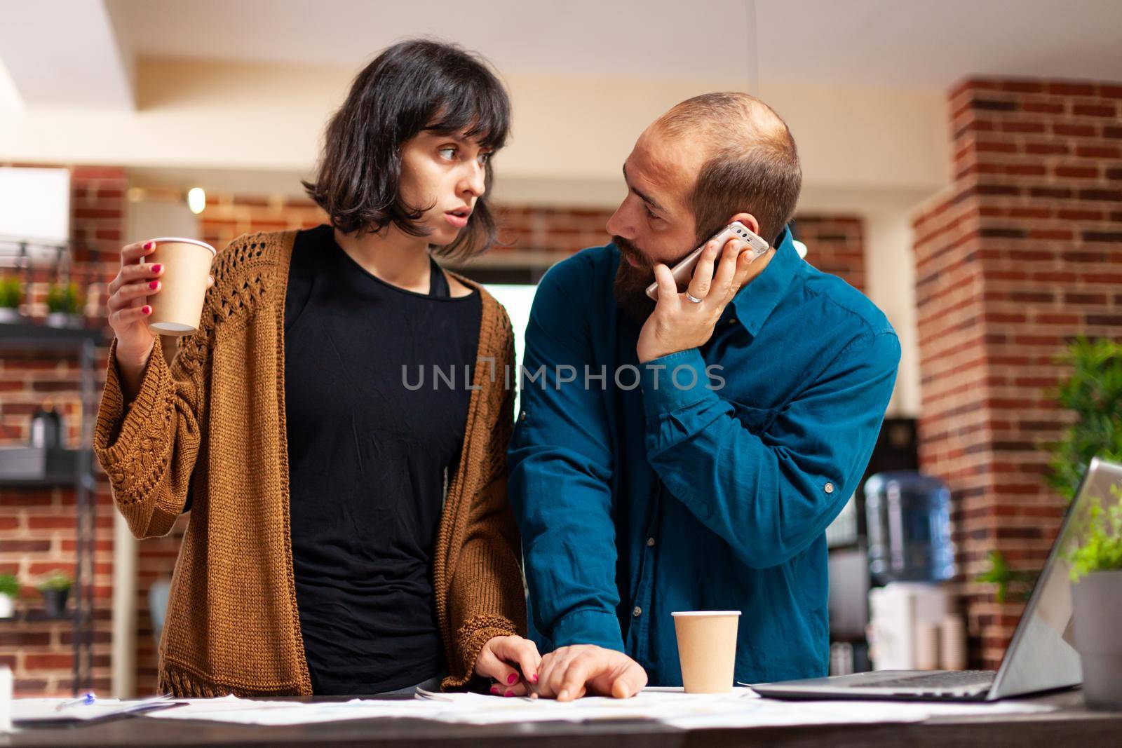 Manager talking at phone with businessman discussing marketing strategy while working at company presentation with entrepreneur woman in startup office. Businesspeople analyzing business document