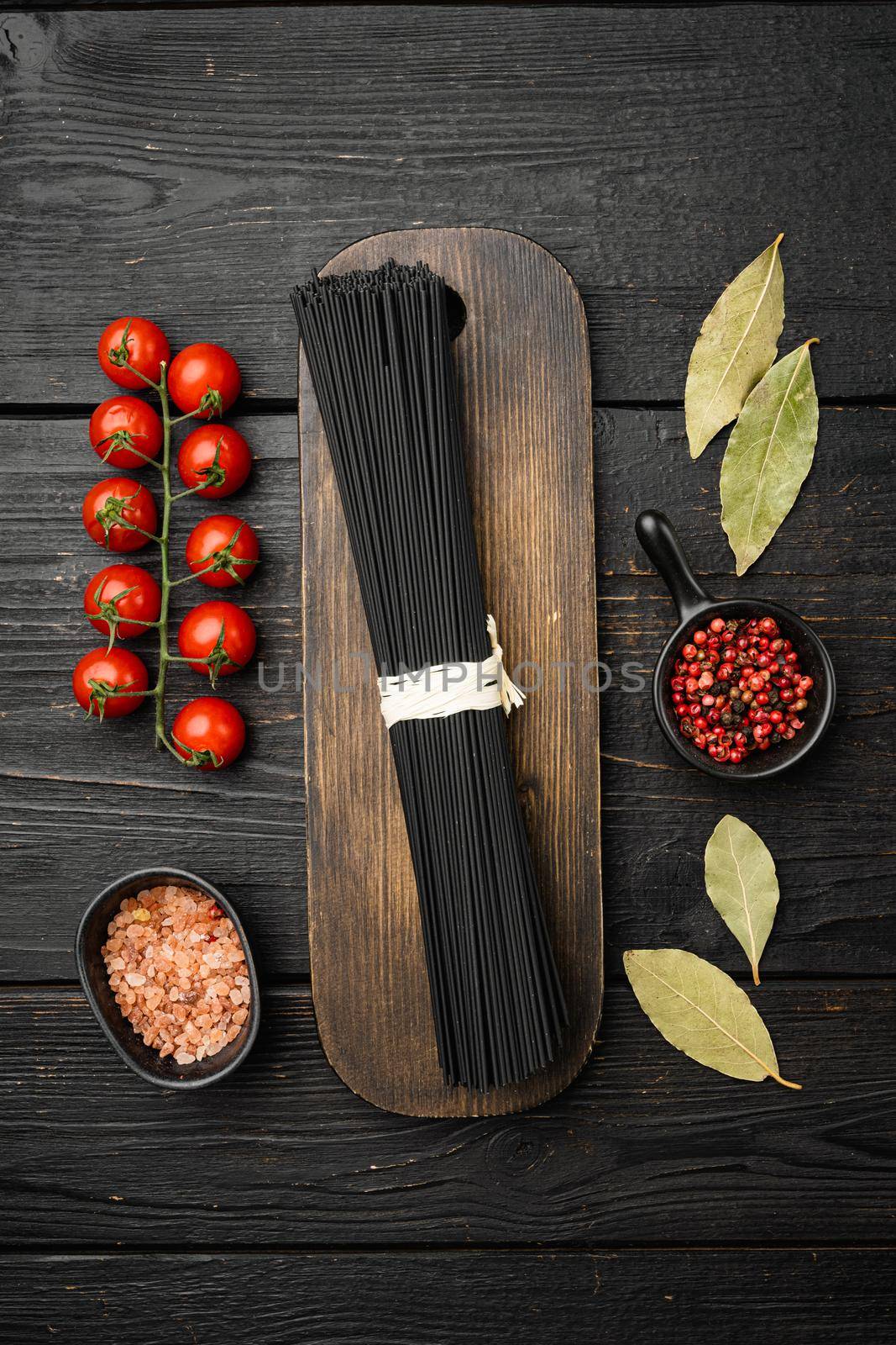 Squid ink black tinted twirl of raw tagliatelle, on black wooden table background, top view flat lay by Ilianesolenyi