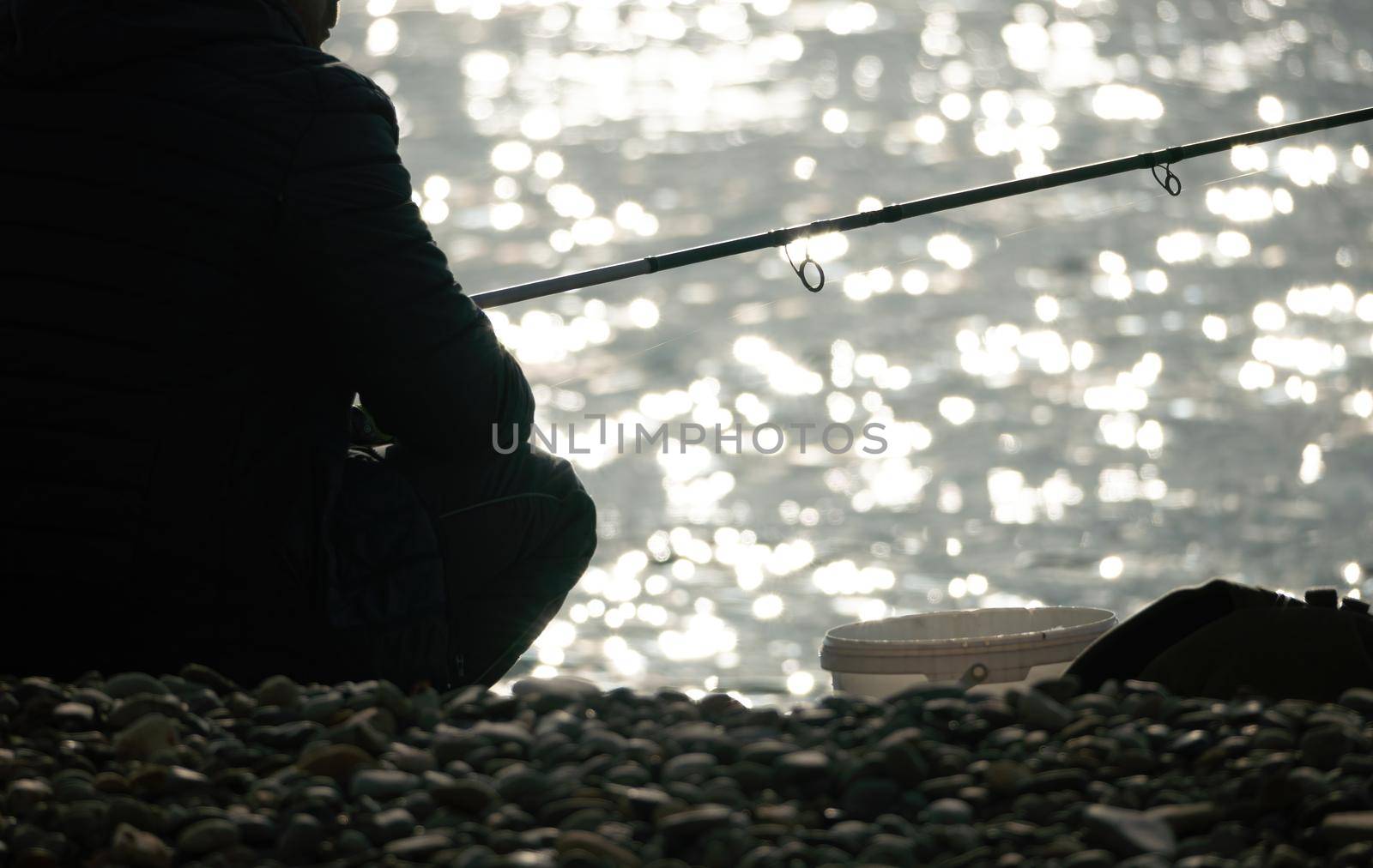 Man hobby fishing on sea tightens a fishing line reel of fish. Calm surface sea. Close-up of a fisherman hands twist reel with fishing line on a rod. Fishing in the blue sea outdoors. by panophotograph