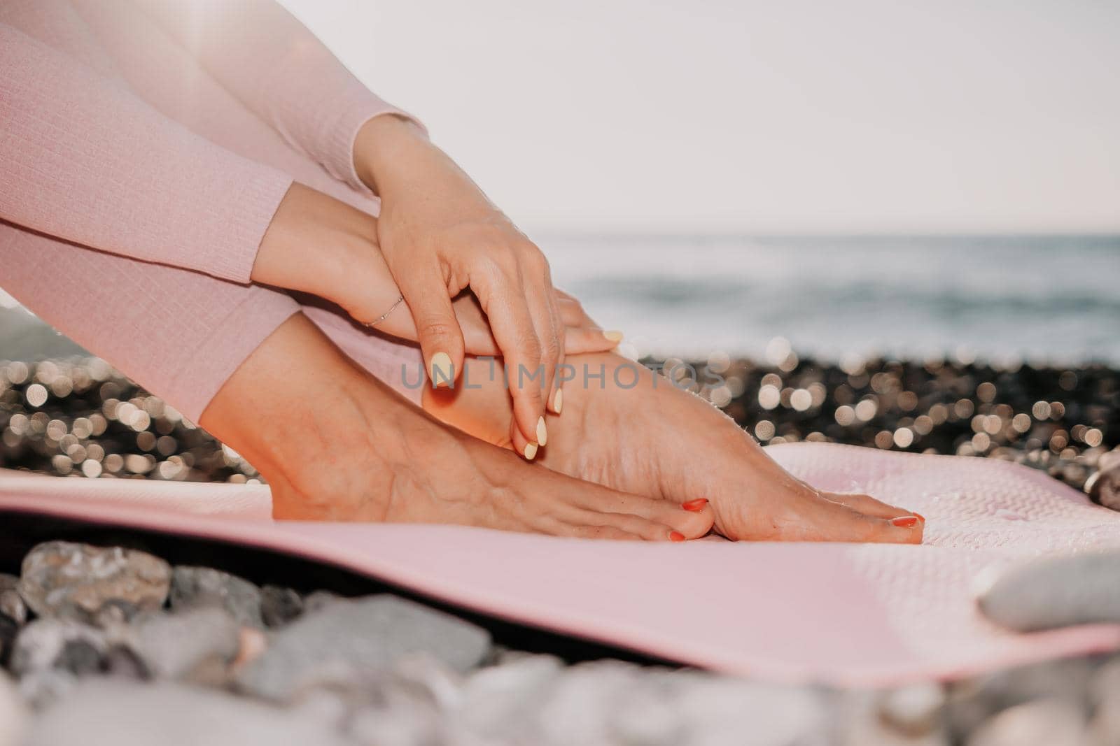 Middle aged well looking woman with black hair doing Pilates with the ring on the yoga mat near the sea on the pebble beach. Female fitness yoga concept. Healthy lifestyle, harmony and meditation. by panophotograph