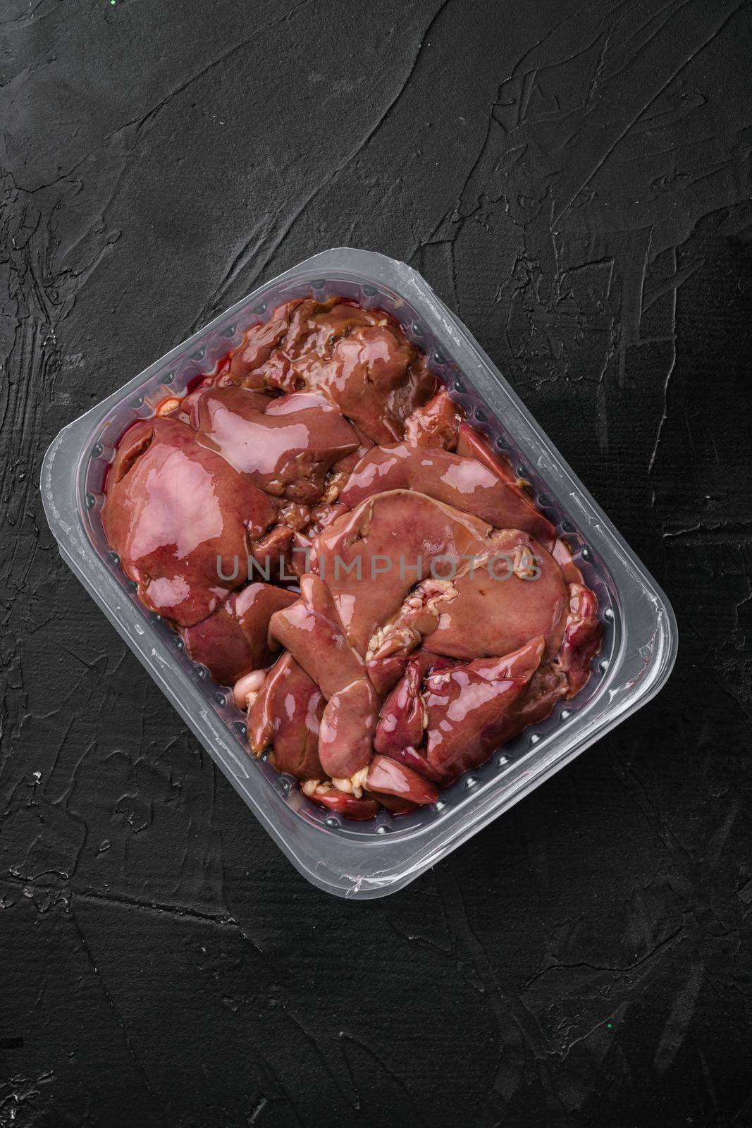 Raw chicken liver in the industrial pack set, on black dark stone table background, top view flat lay, with copy space for text