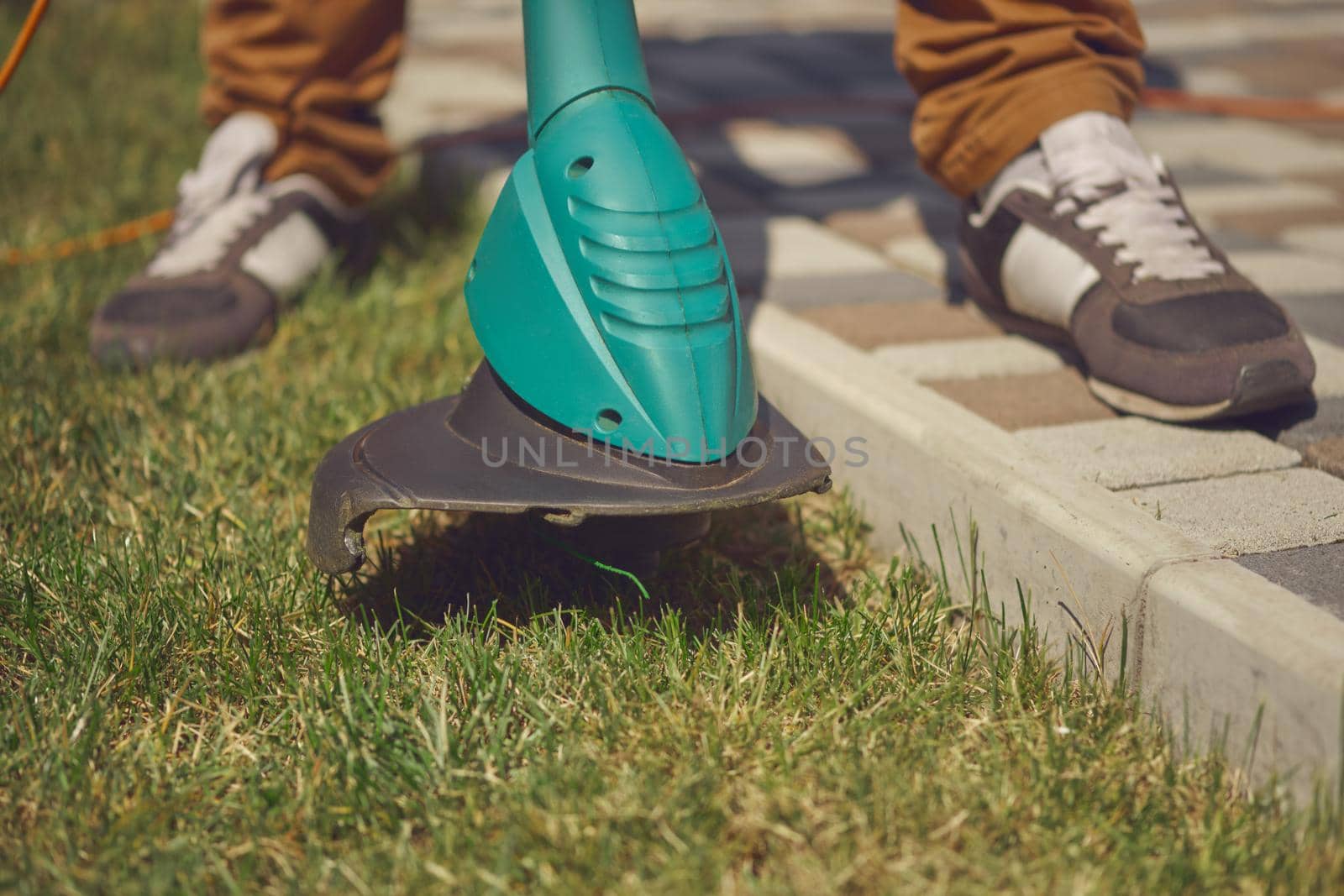 Male in sneakers and pants is cutting green grass with handheld modern lawn mower in his garden. Gardening care equipment and services. Close up by nazarovsergey