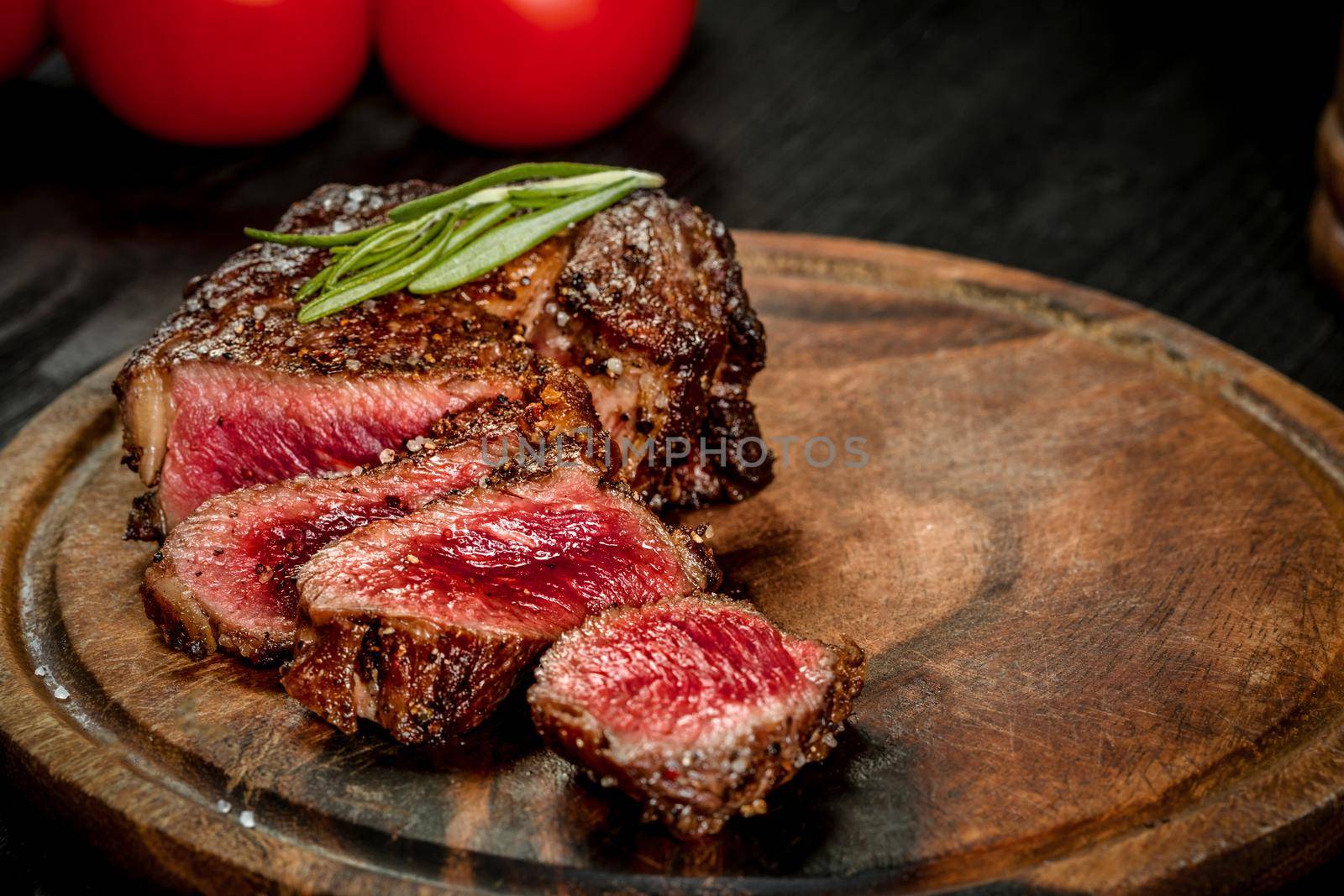 Grill juicy beef steak with salt pepper and rosemary on a wooden board with a knife and fork. Still life