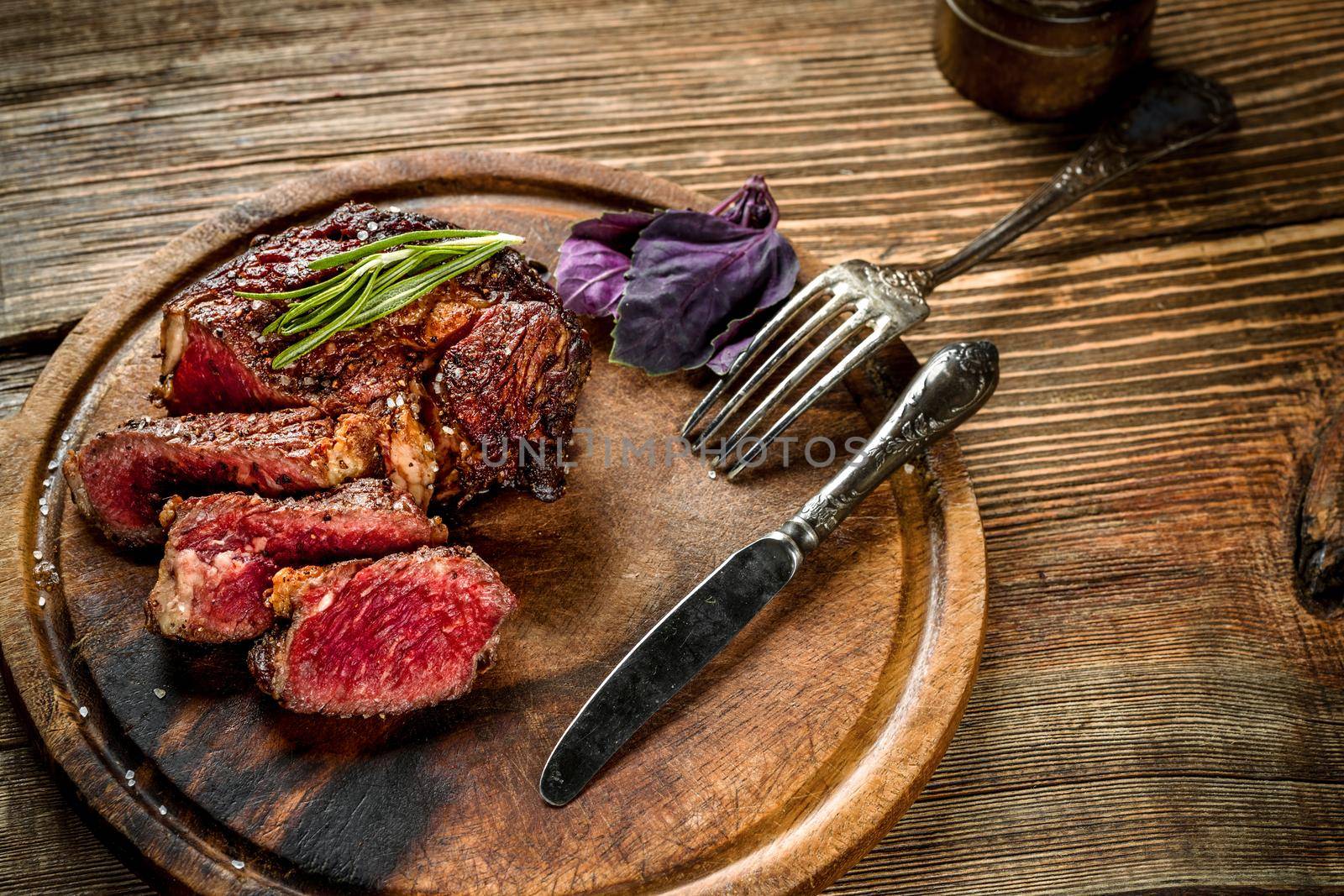 Grill juicy beef steak with salt pepper and rosemary on a wooden board with a knife and fork. Still life