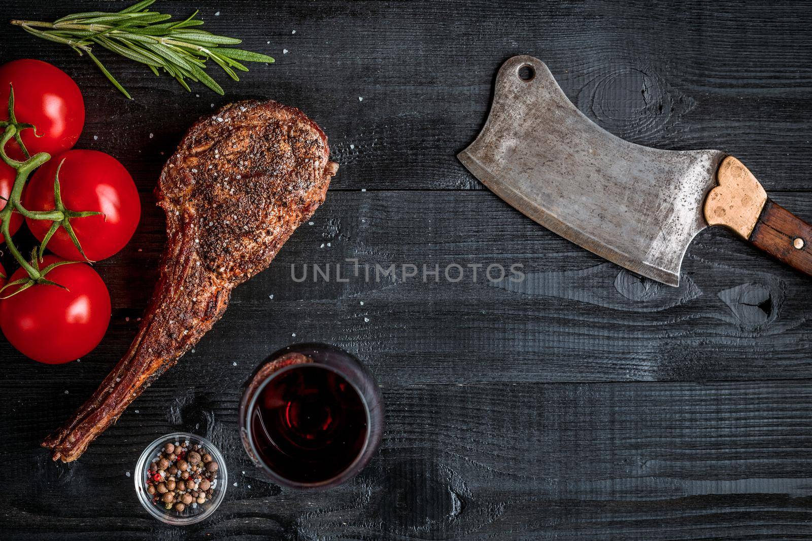 Barbecue dry aged rib of beef with spice, vegetables and glass of red wine close-up on black wooden background. Top view. Copy space. Still life. Flat lay