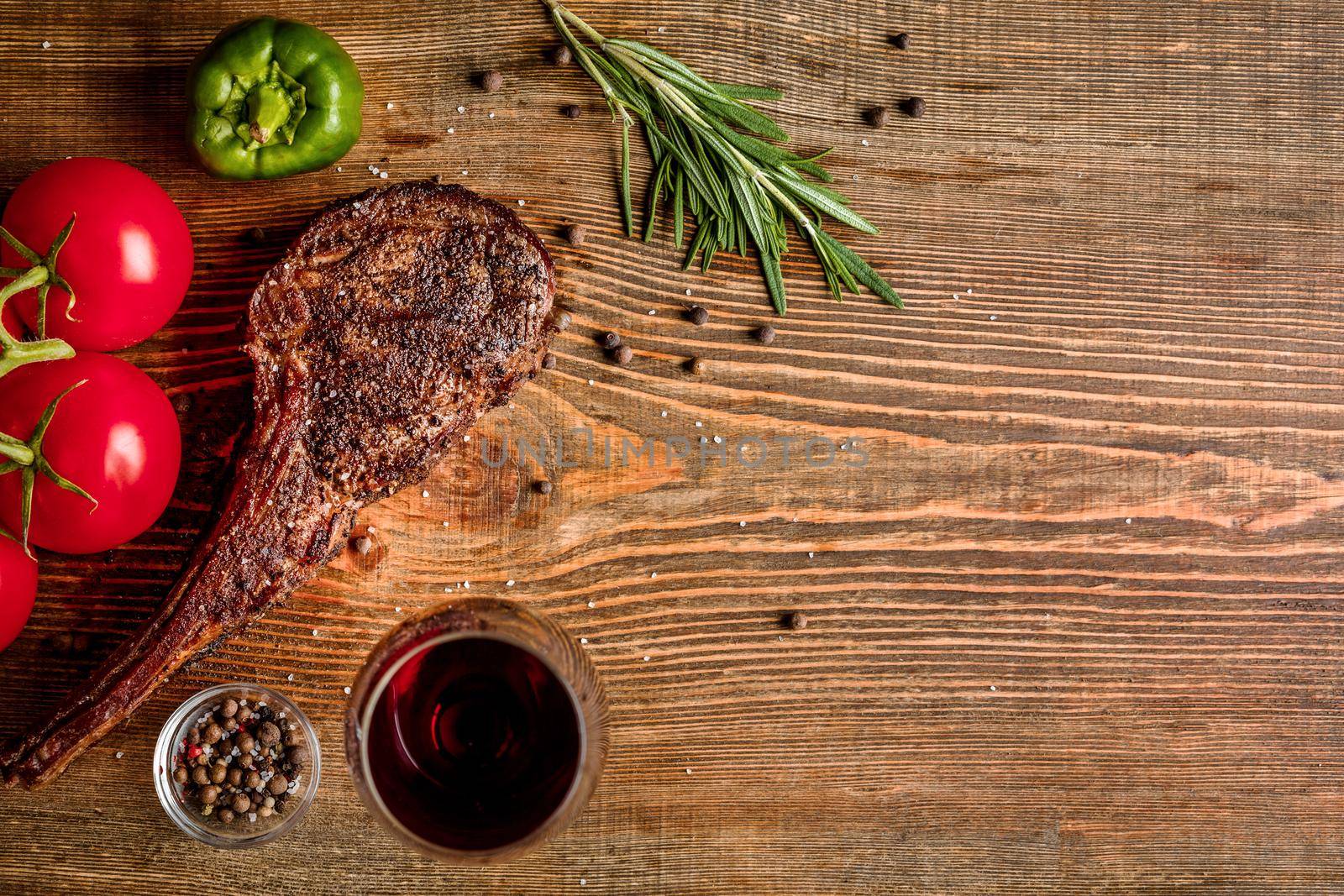 Barbecue dry aged rib of beef with vegetables and glass of red wine close-up on wooden background by nazarovsergey