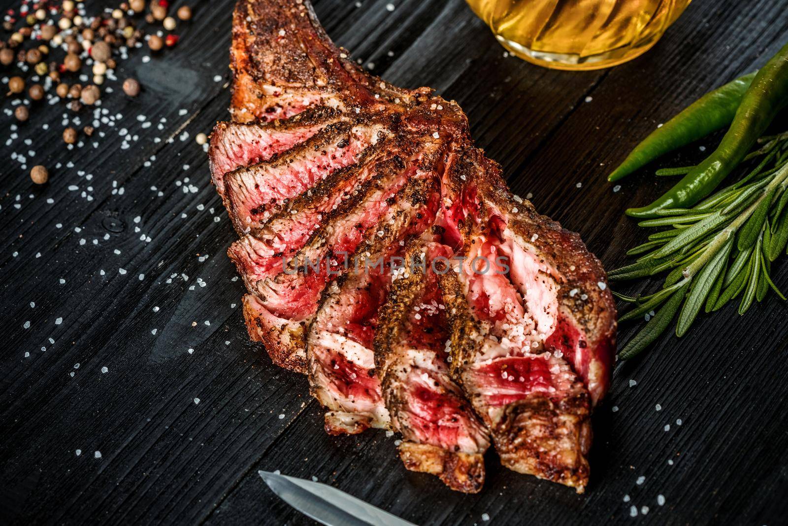 Barbecue dry aged rib of beef with spice, vegetables and a glass of light beer close-up on black wooden background. Top view. Copy space. Still life. Flat lay