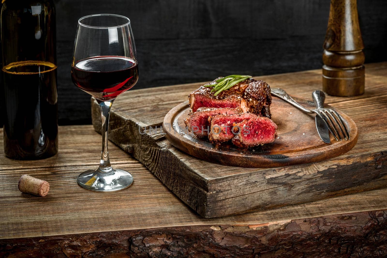 Grilled ribeye beef steak with red wine, herbs and spices on wooden table. Still life