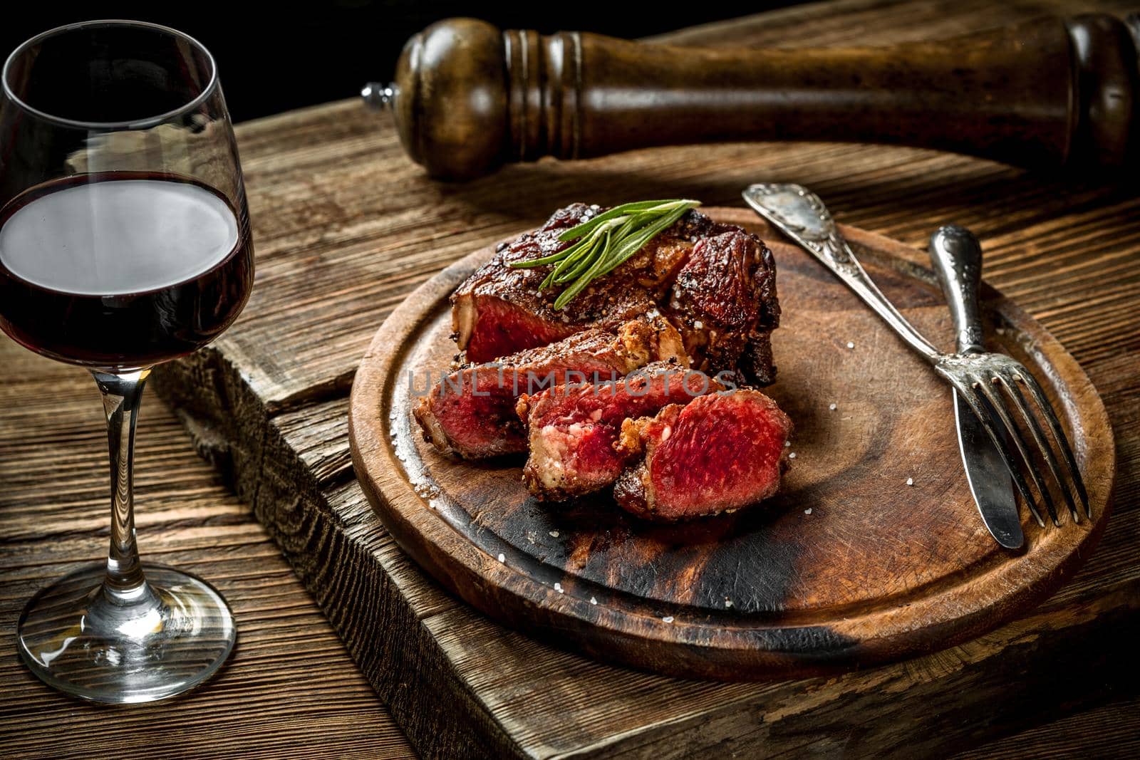 Grilled ribeye beef steak with red wine, herbs and spices on wooden table by nazarovsergey