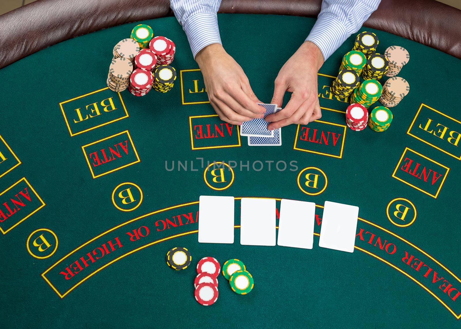 Close up of poker player with playing cards and chips at green casino table, view from above.