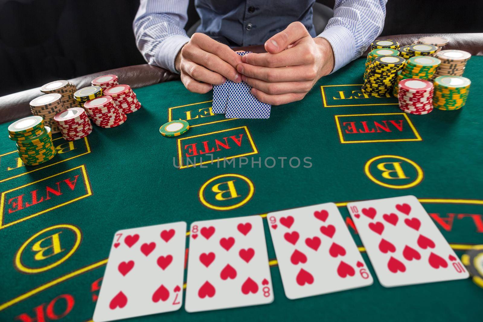 Close up of poker player with playing cards and chips at green casino table