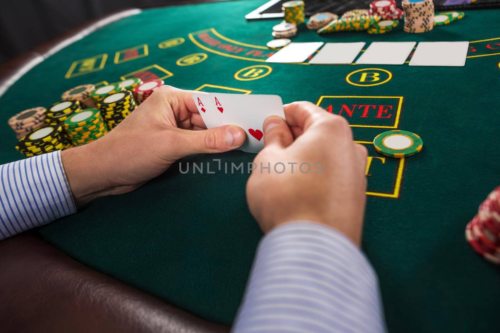 Male poker player holding the of two cards aces at green casino table