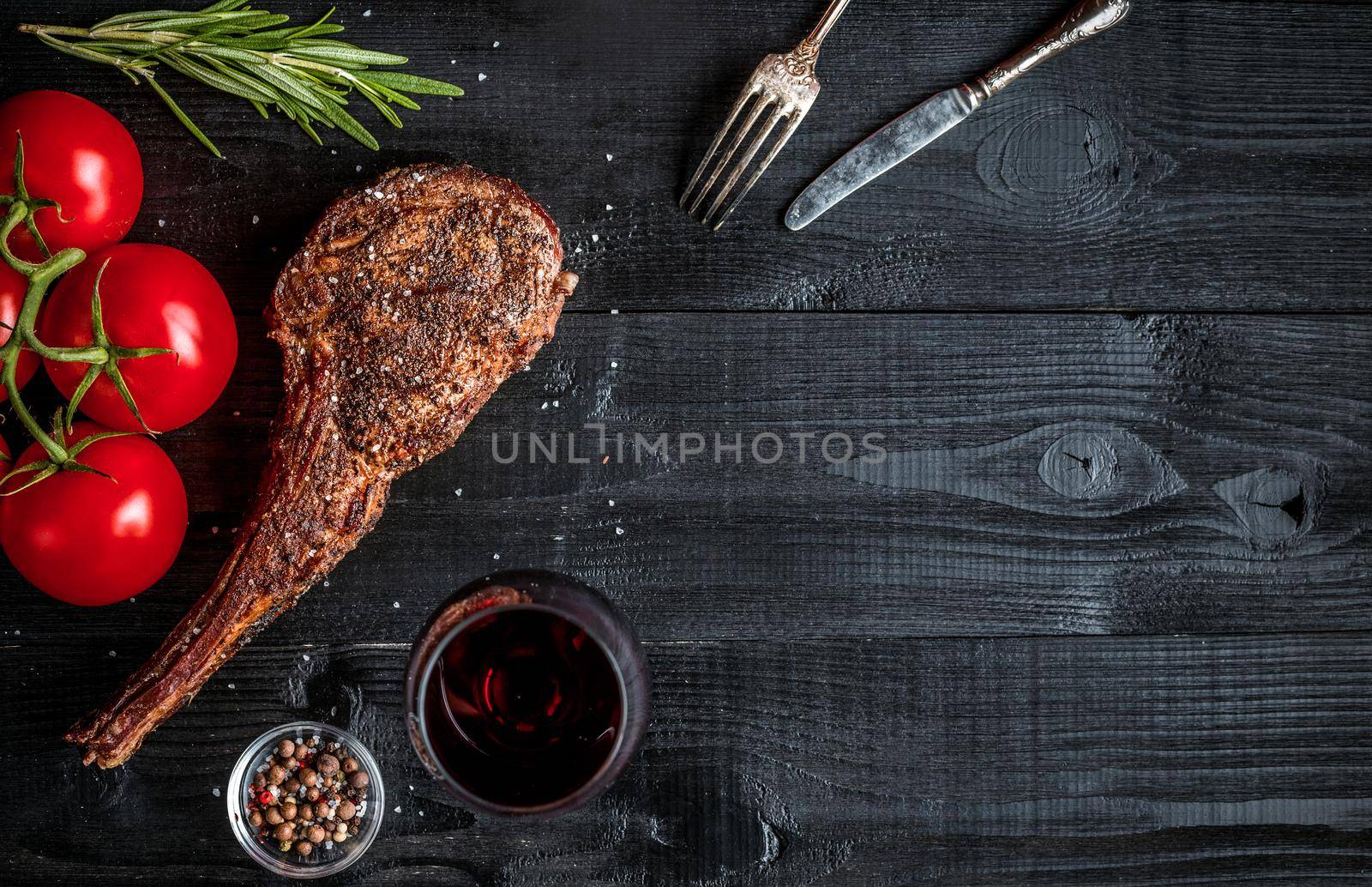 Barbecue dry aged rib of beef with spice, vegetables and glass of red wine close-up on black wooden background. Top view. Copy space. Still life. Flat lay