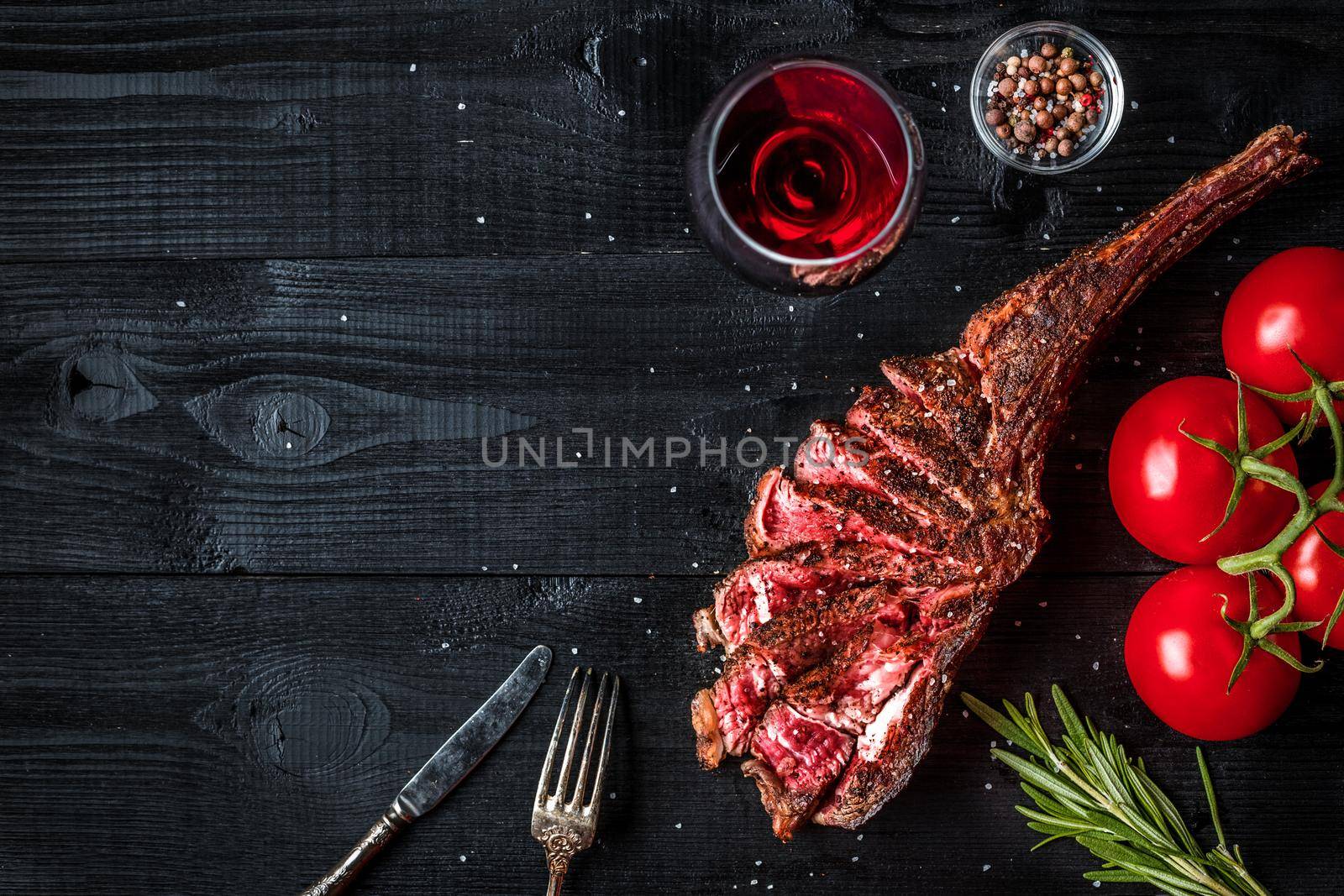 Barbecue dry aged rib of beef with spice, vegetables and glass of red wine close-up on black wooden background. Top view. Copy space. Still life. Flat lay