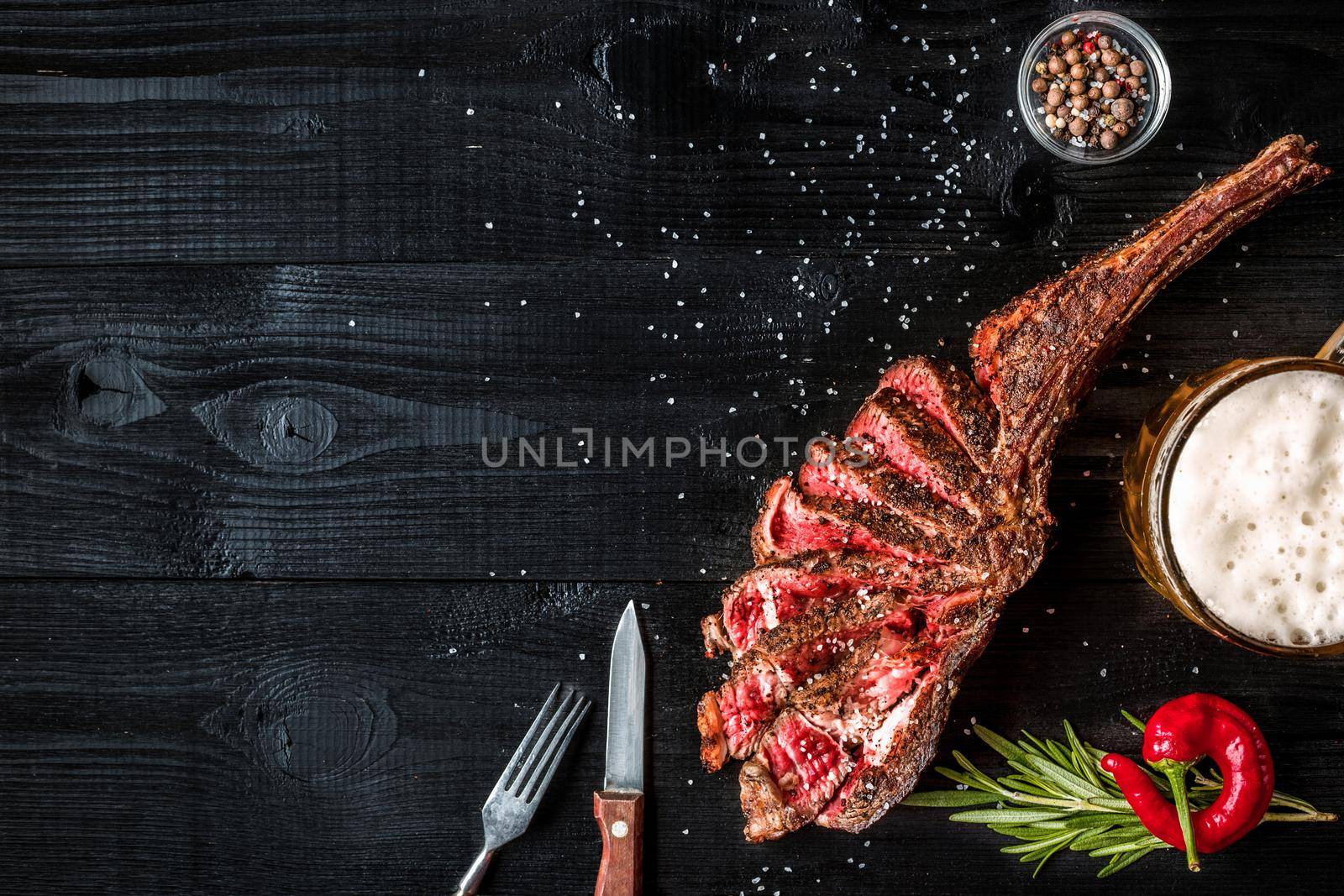 Barbecue dry aged rib of beef with spice, vegetables and a glass of light beer close-up on black wooden background by nazarovsergey