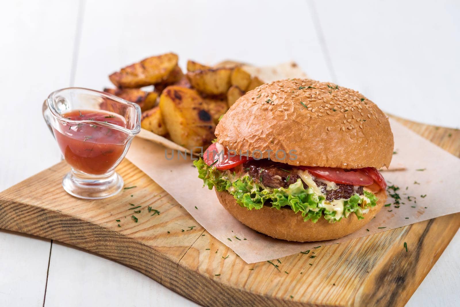 Fast food dish. Appetizing meat burger, potato chips and sauce. Takeaway composition. French fries, hamburger and sauce on wooden board.