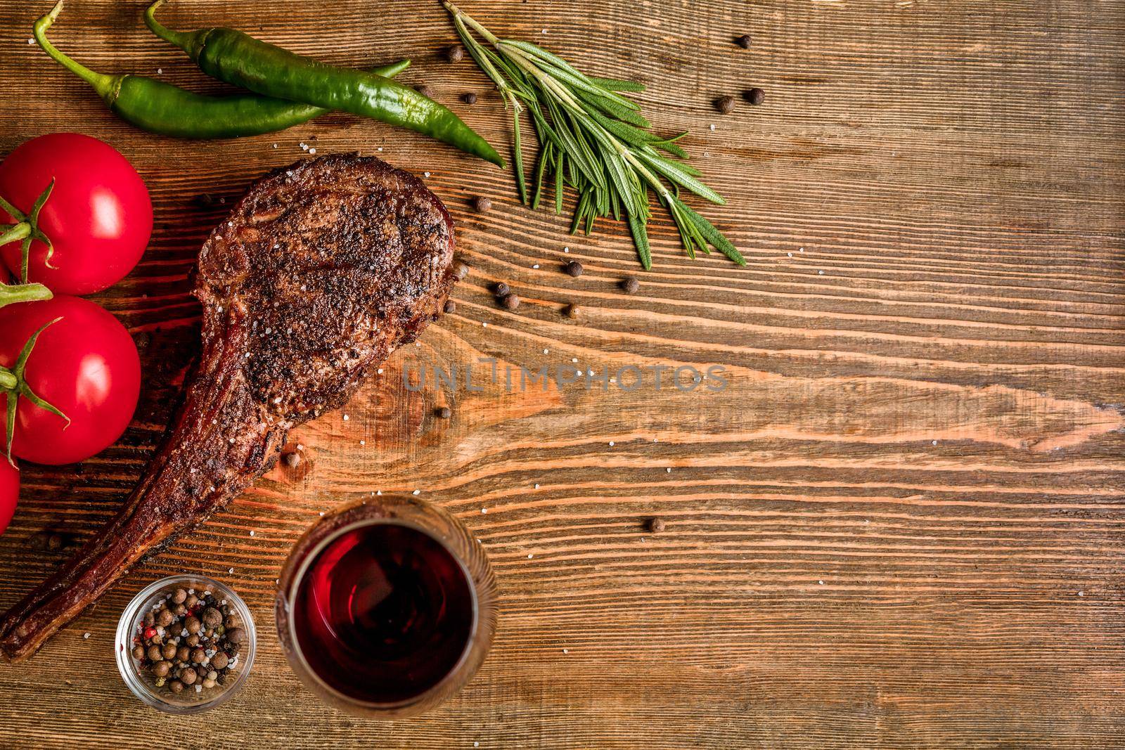 Barbecue dry aged rib of beef with vegetables and glass of red wine close-up on wooden background by nazarovsergey