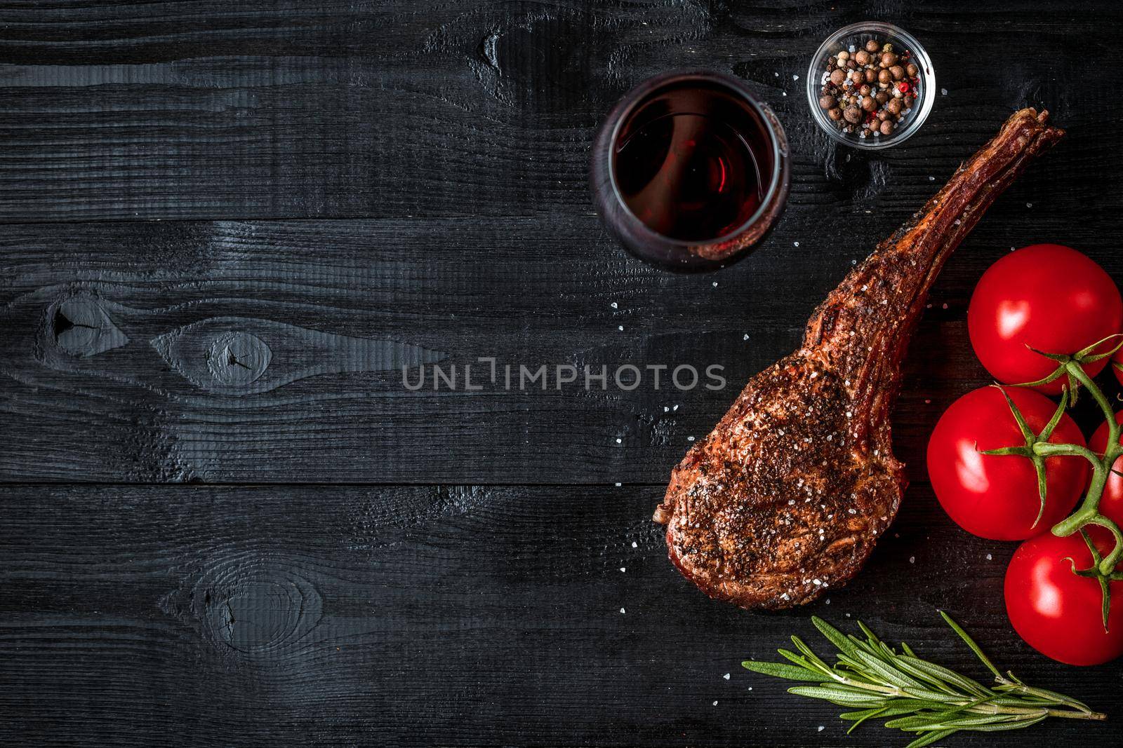 Barbecue dry aged rib of beef with spice, vegetables and glass of red wine close-up on black wooden background. Top view. Copy space. Still life. Flat lay