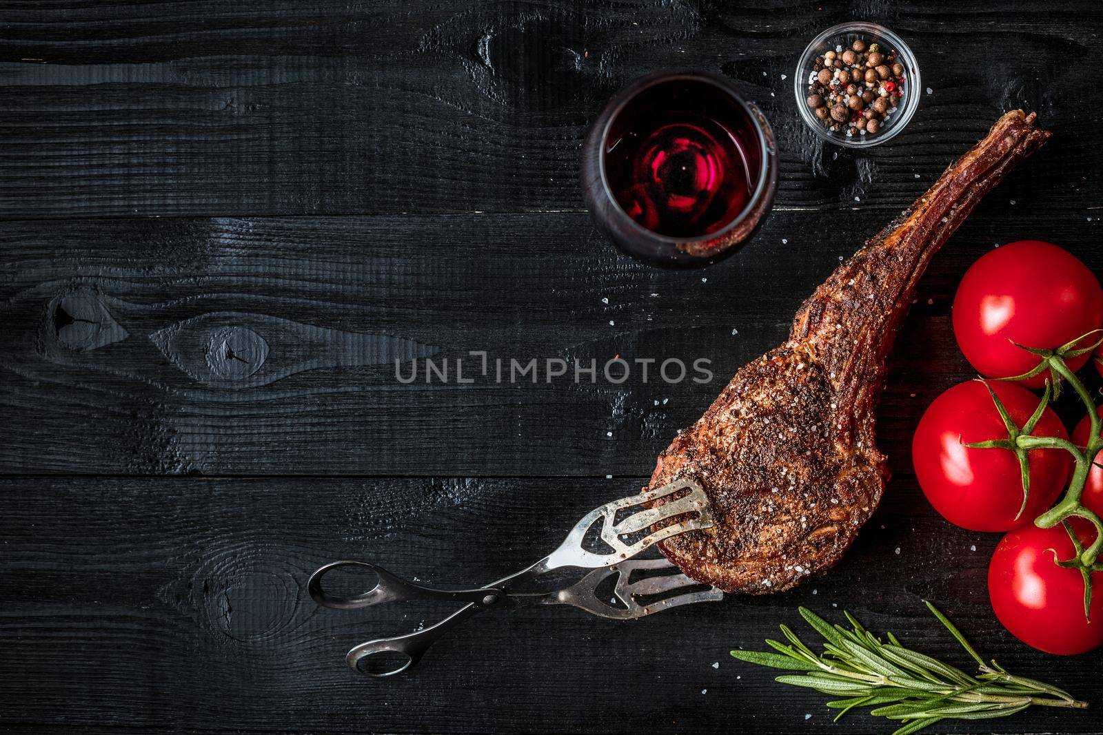 Barbecue dry aged rib of beef with spice, vegetables and glass of red wine close-up on black wooden background. Top view. Copy space. Still life. Flat lay