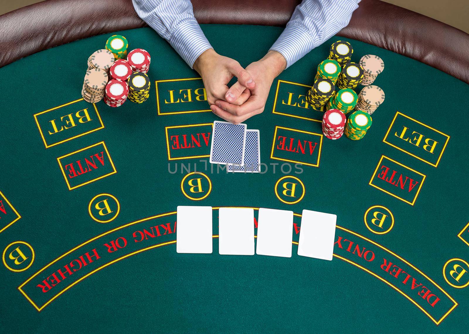 Close up of poker player with playing cards and chips at green casino table, view from above.