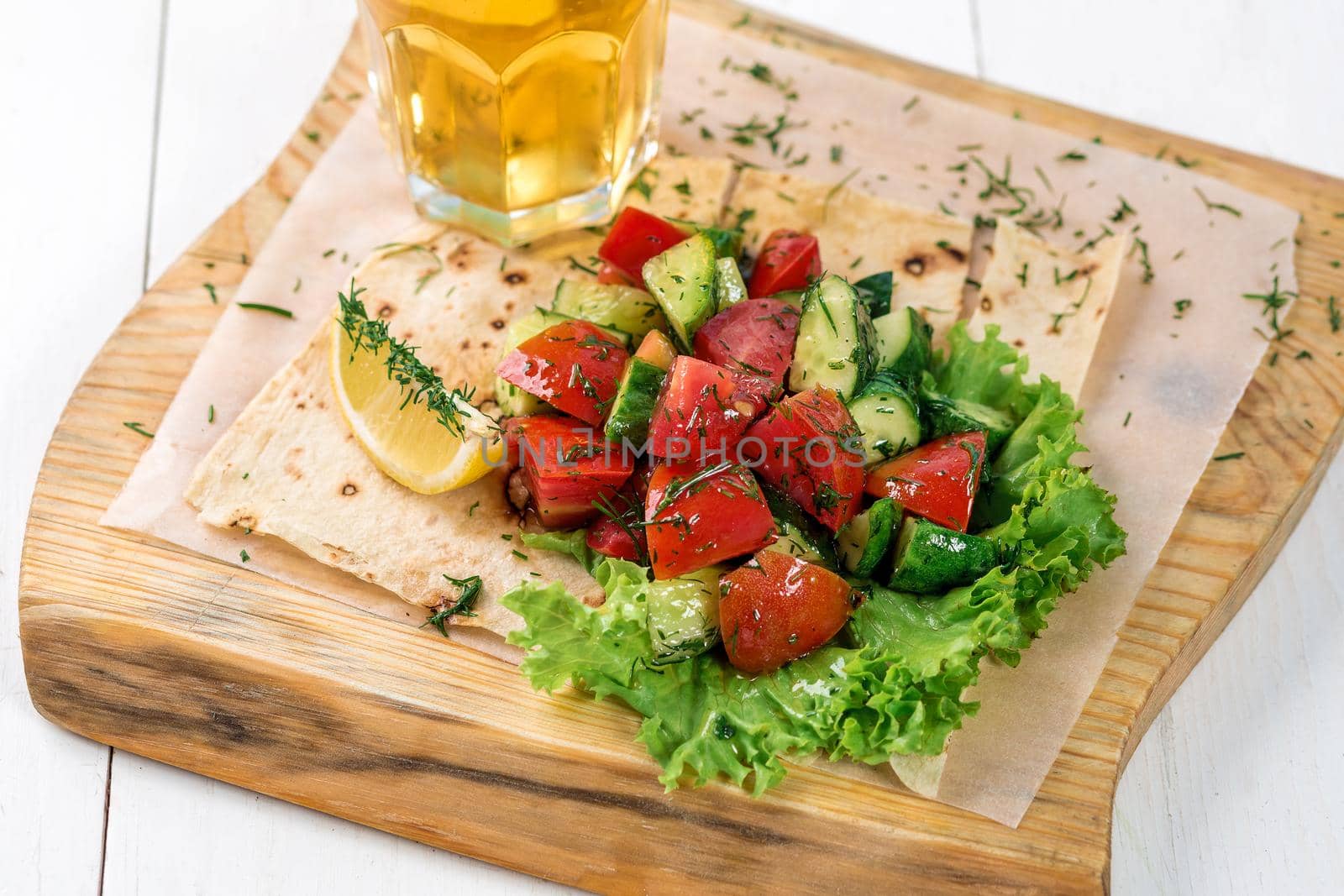 Vegetable salad with greens on a wooden board. A glass of light beer and salad on a white wooden table