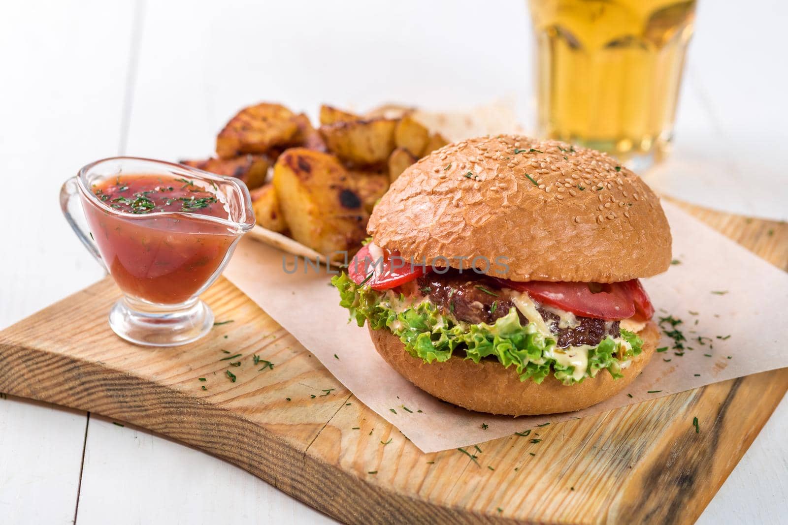 Fast food dish. Appetizing meat burger, potato chips and sauce. Takeaway composition. French fries, hamburger and sauce on wooden board.