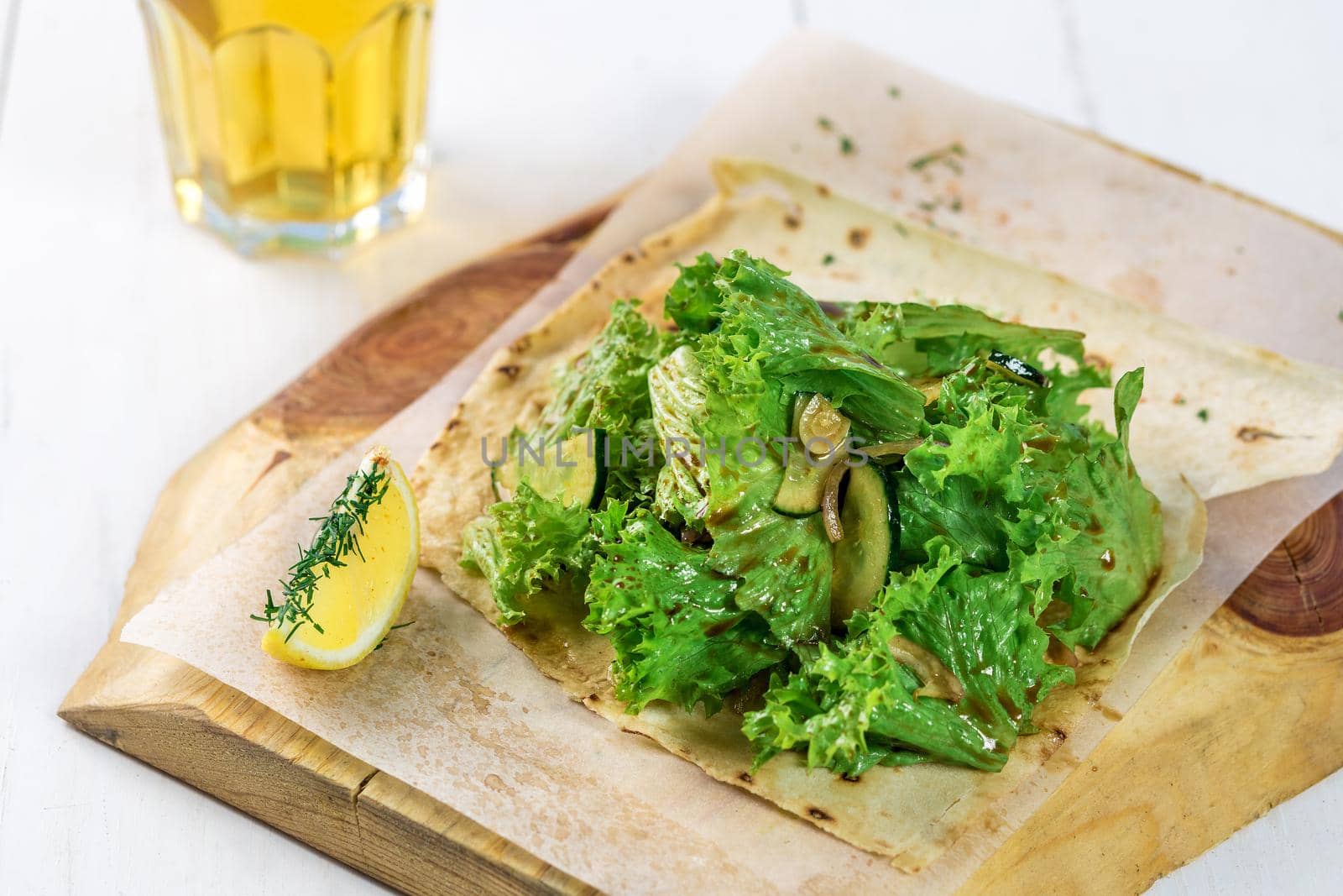 Vegetable salad with greens on a wooden board. A glass of light beer and salad on a white wooden table