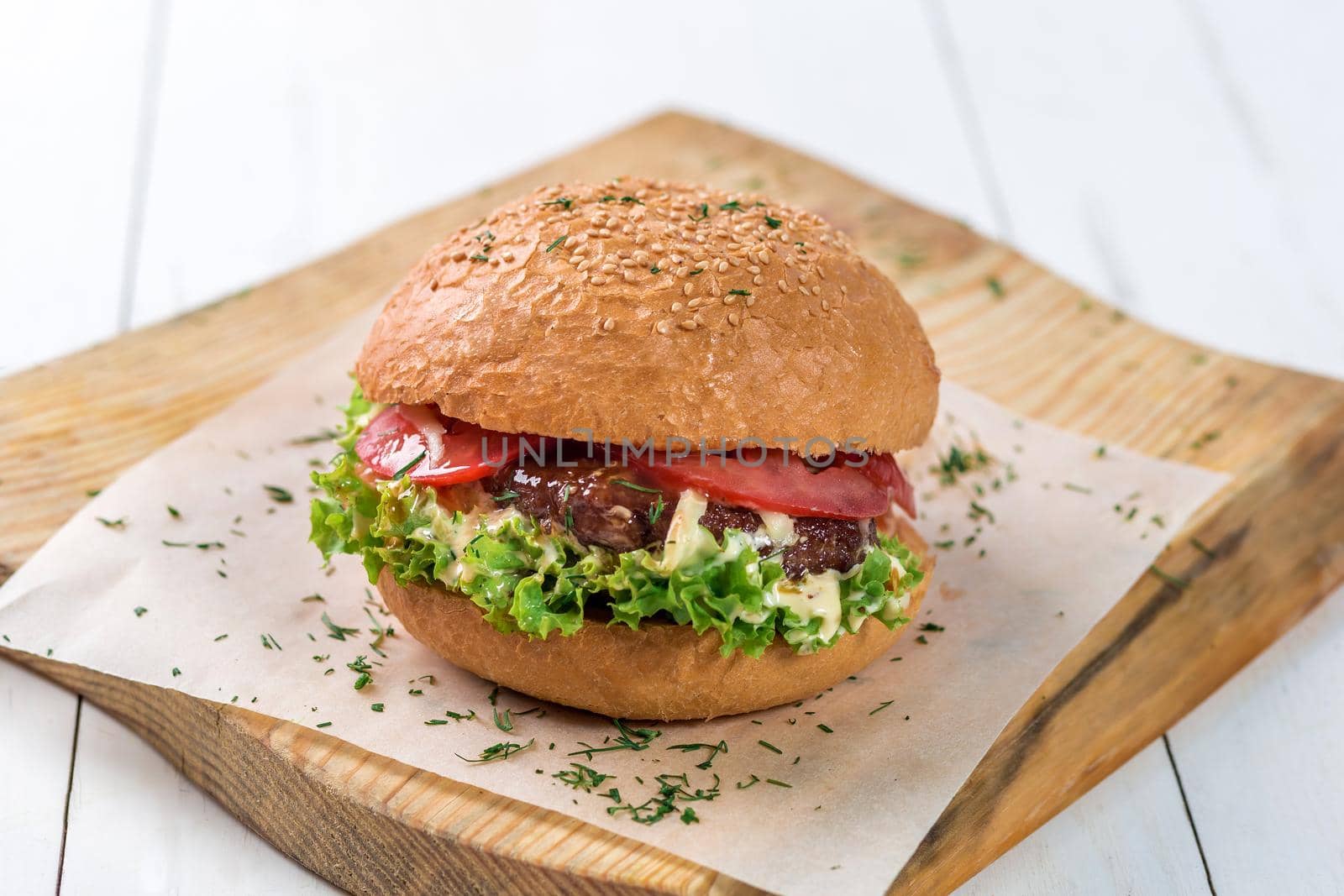 Close-up of home made burger on wooden board. A white wooden table